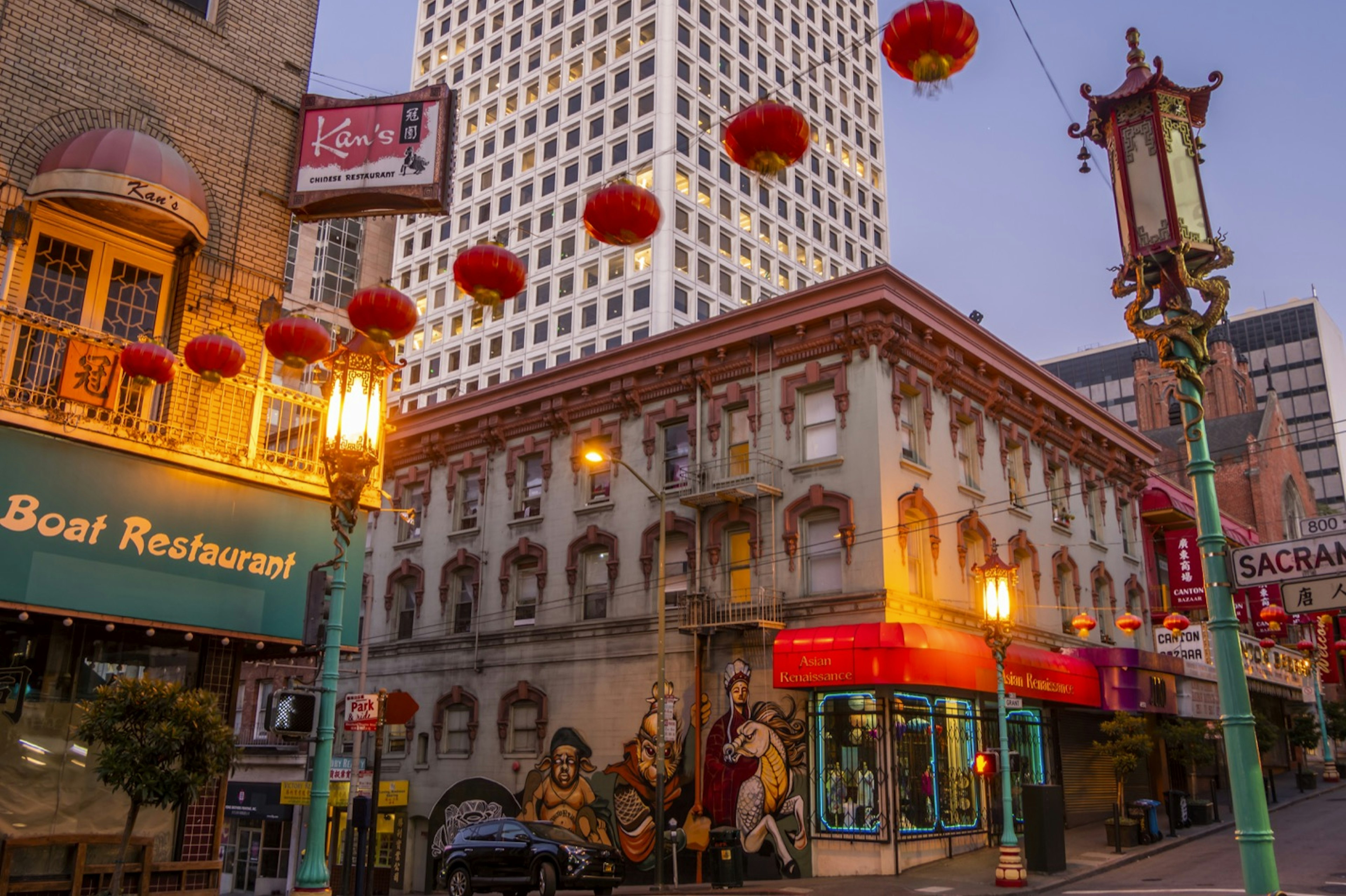 Red lanterns hang over a street lined with street lights adorned in dragons a victorian building on the corner is adorned with a mural . Weekend in San Francisco