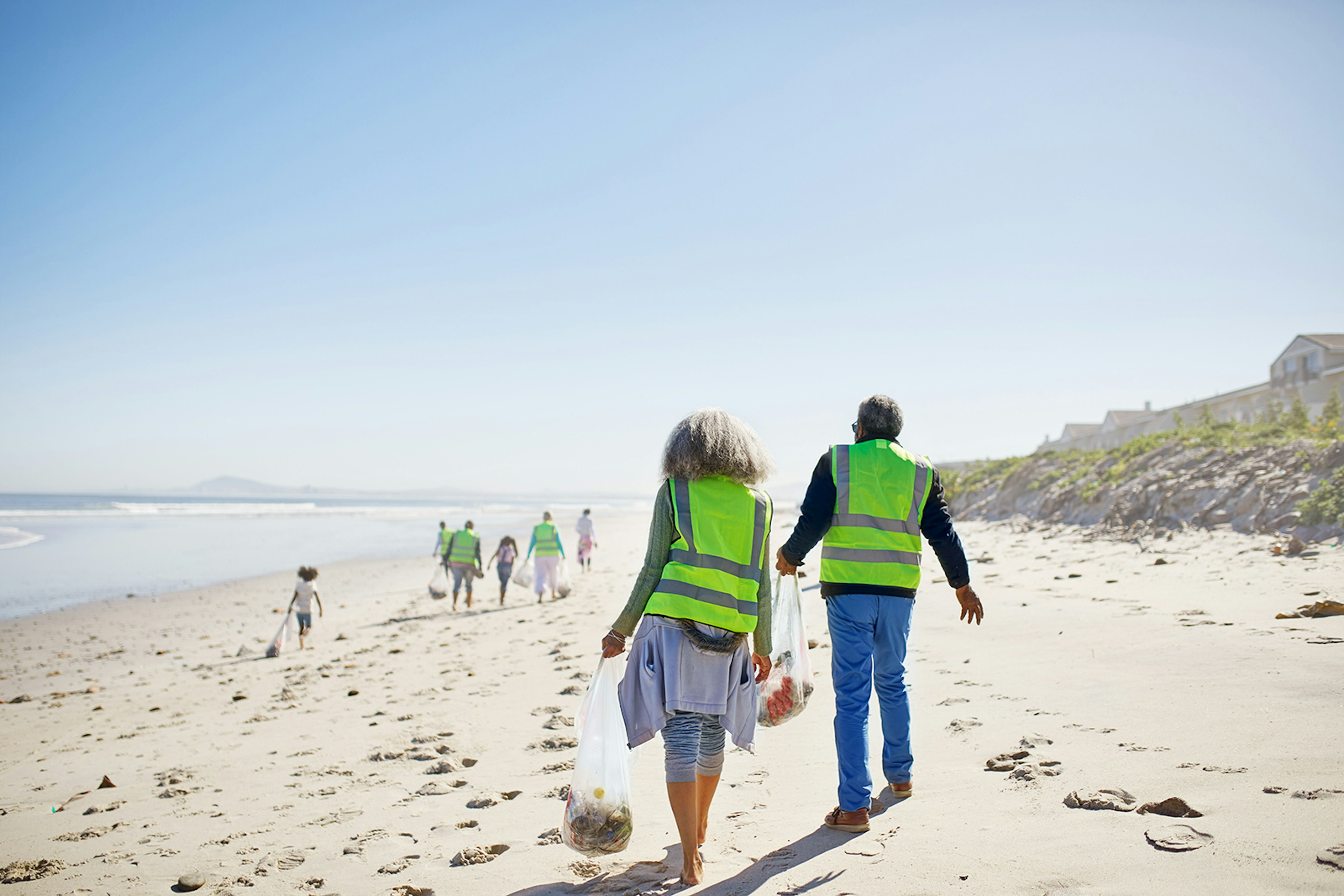 Volunteers wearing high-vis vests cleaning up a white-sand beach on a sunny day