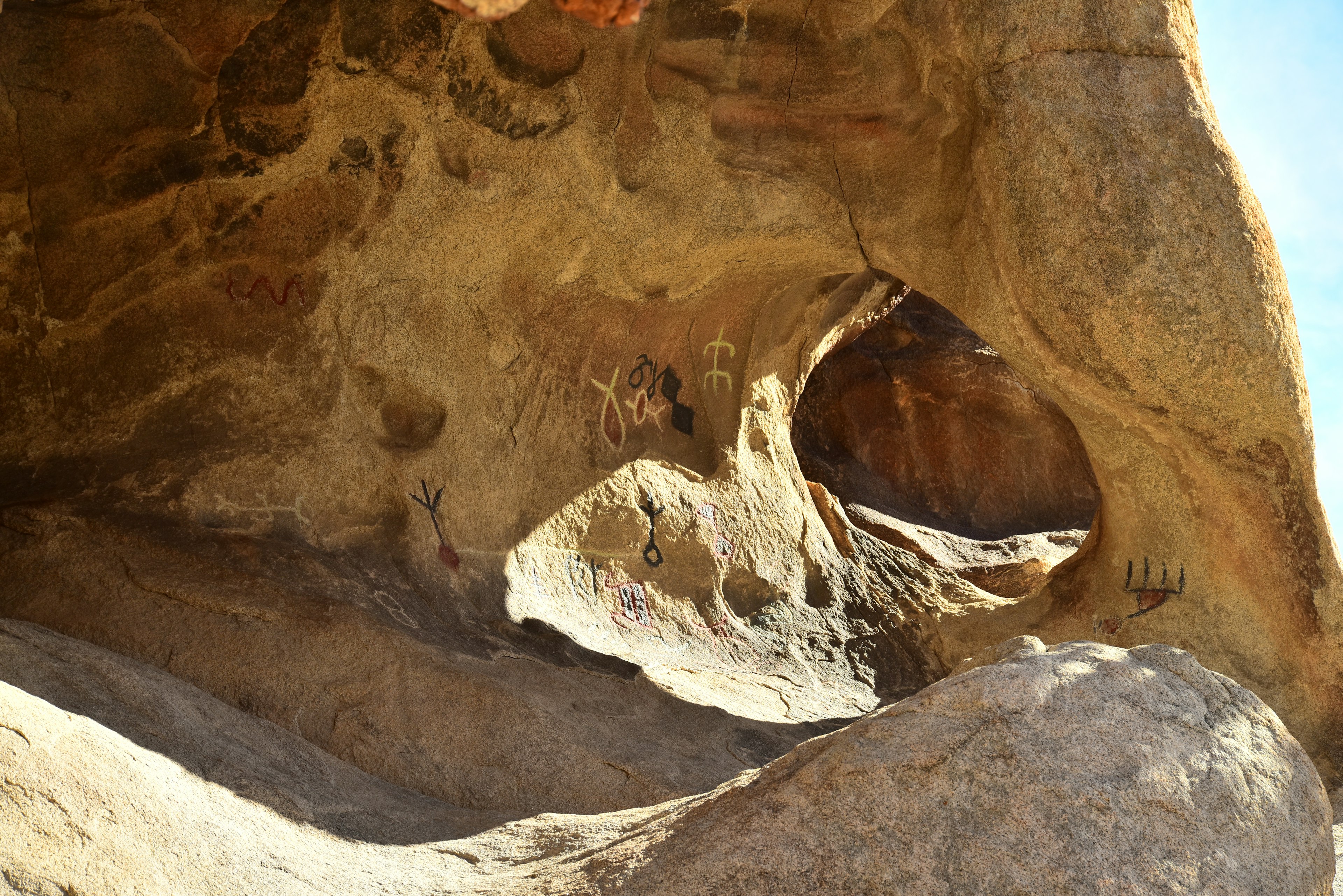 Ancient indigenous petroglyphs mark a rock with a shallow arch in Joshua Tree National Park.