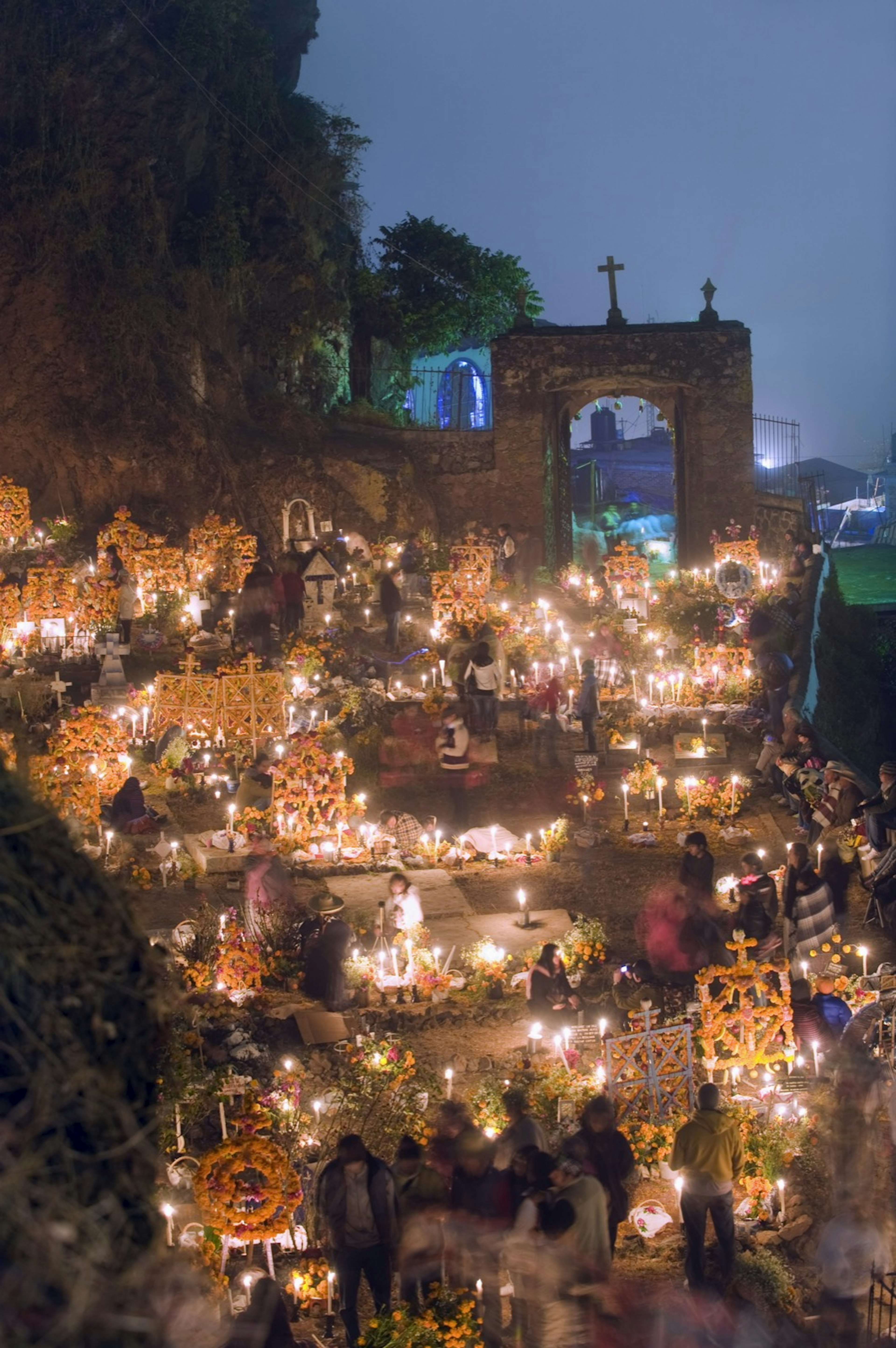 A cemetery with tombs decorated in vibrant yellow flowers is illuminated by candlelight; dia de Muertos