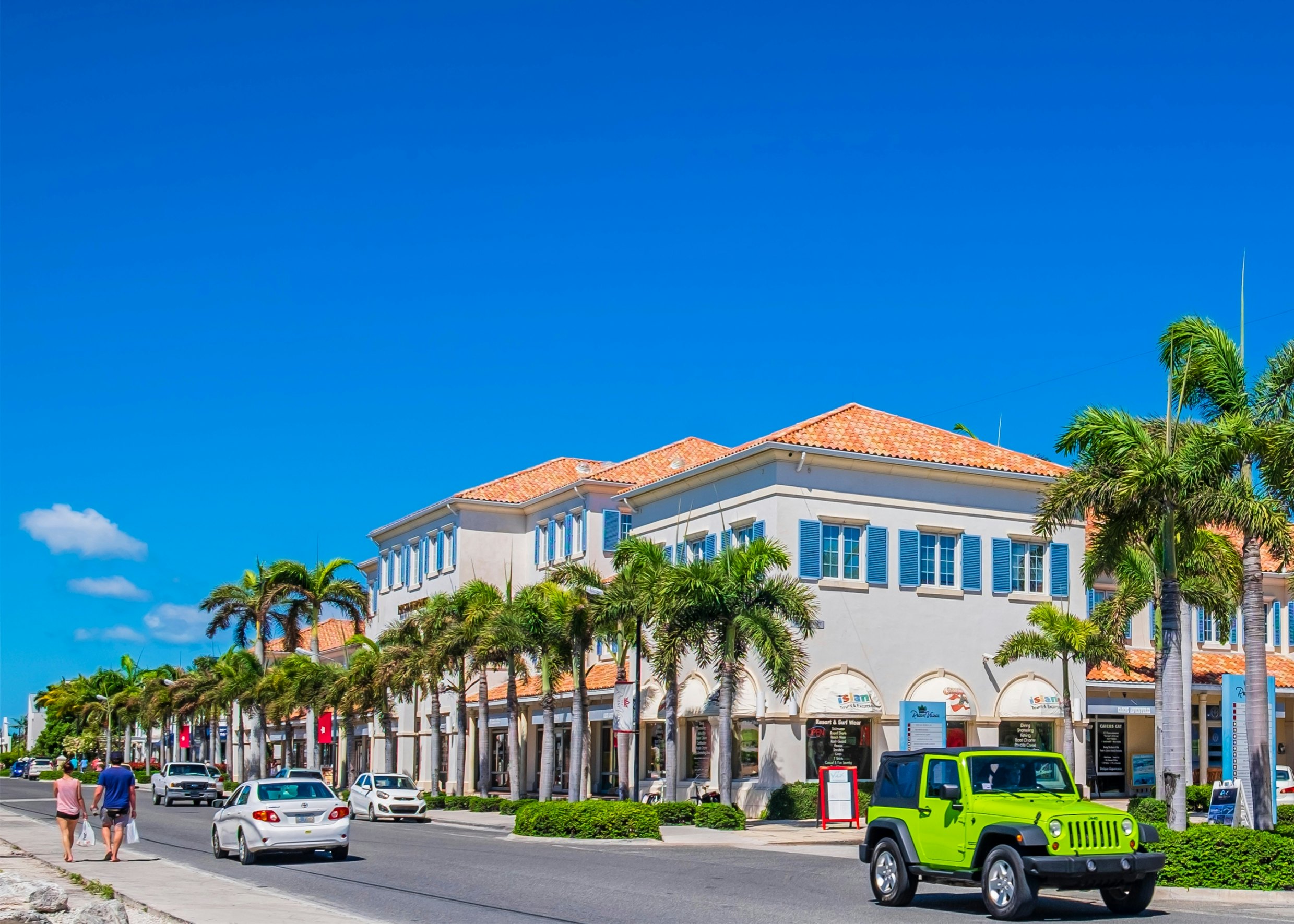 People walk along a street that's lined with tall palm trees shading upmarket stores.| There are plenty of shops to peruse, including those at the Regent Village (pictured), with prices on par with the US. Orietta Gaspari/Getty Images