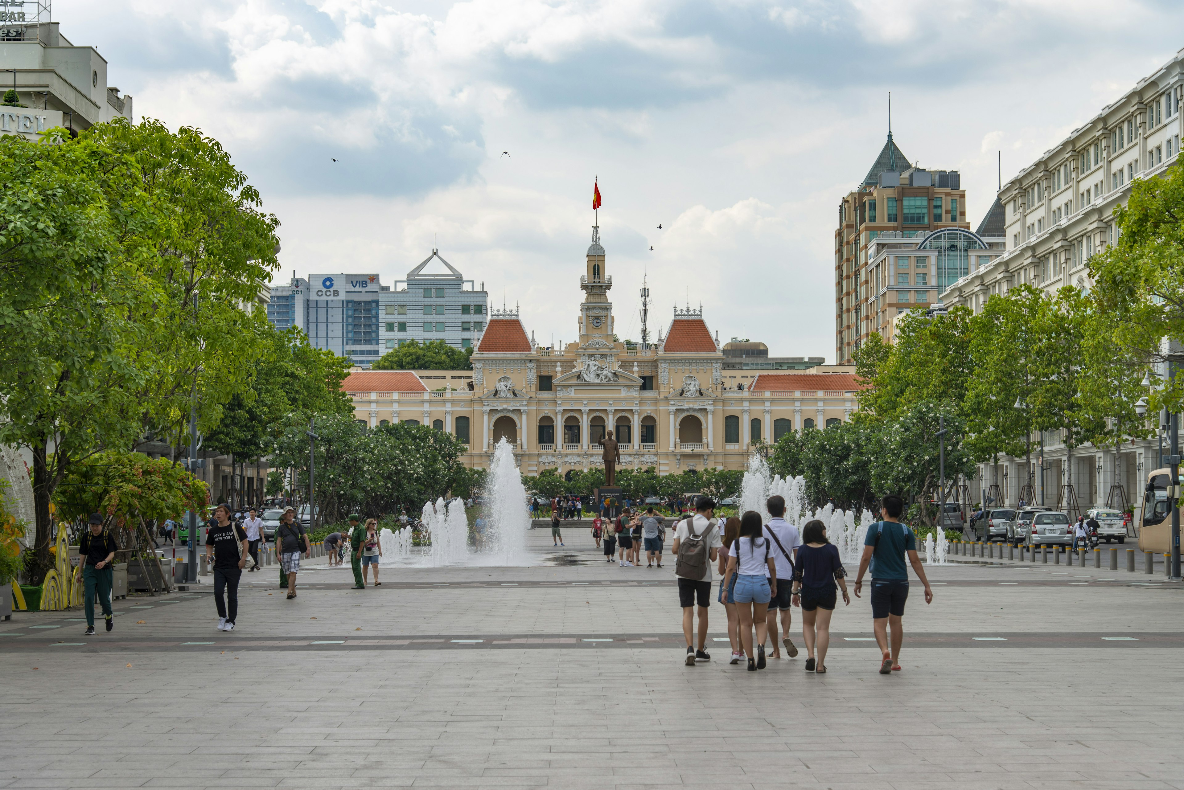 People walk down the middle of the street in front of a large municipal building in a city center