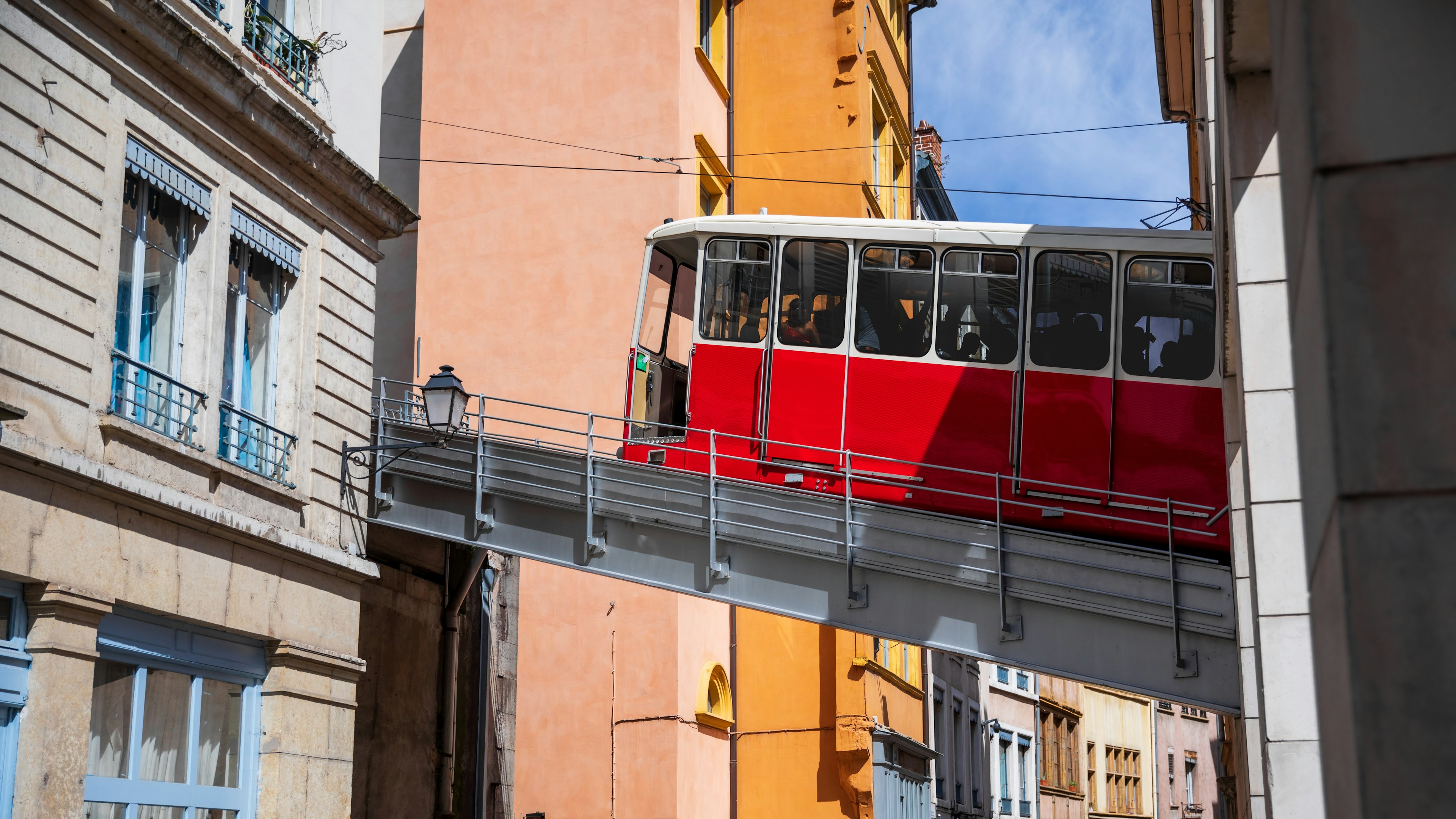 A red funicular train passes between buildings on an elevated track in Lyon