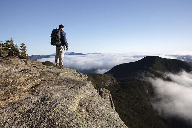 A hiker takes in the view of undercast from the summit of Mount Osceola in the White Mountains, New Hampshire USA