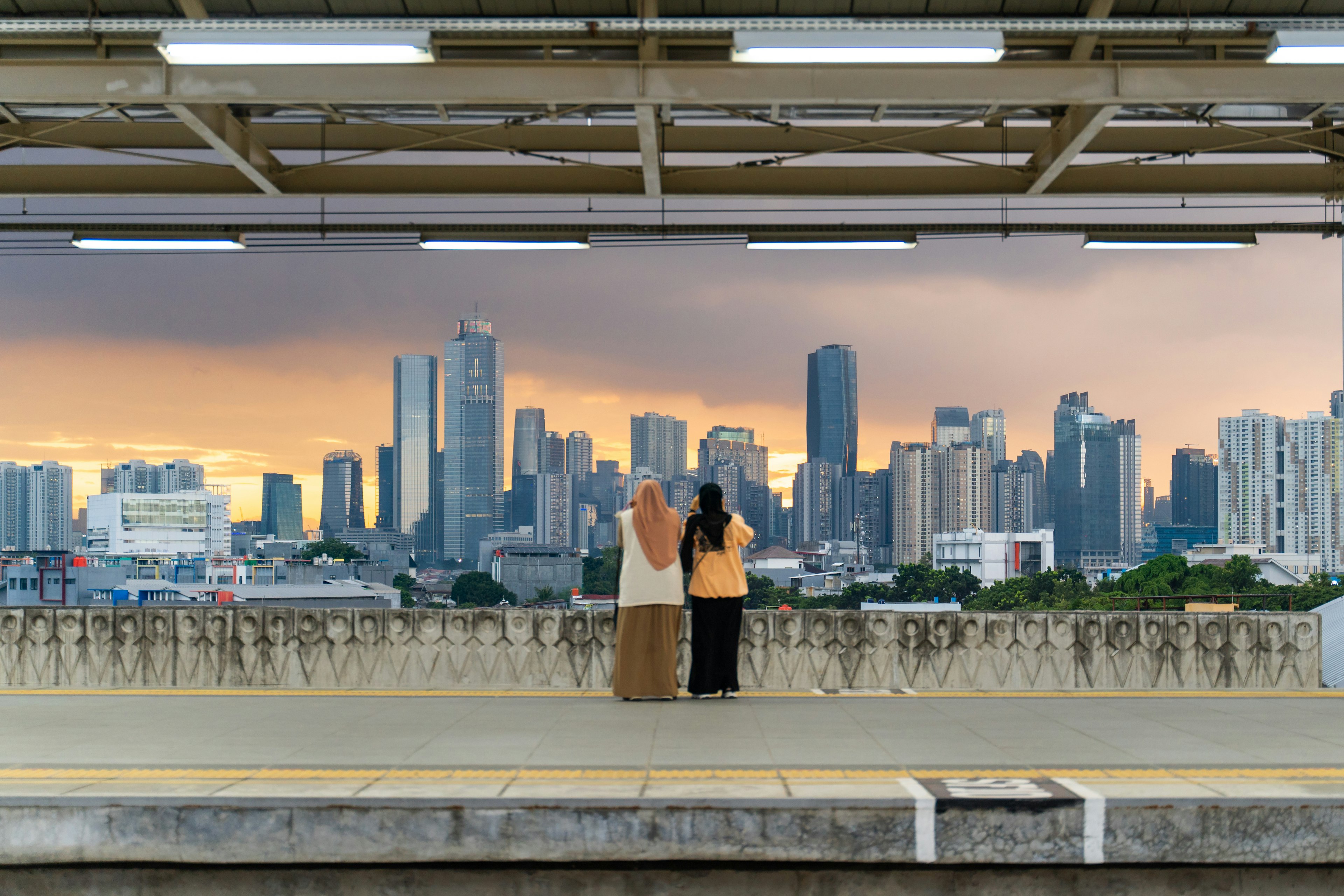 Two Indonesian women watching the city skyline from a train station in Jakarta, Indonesia.