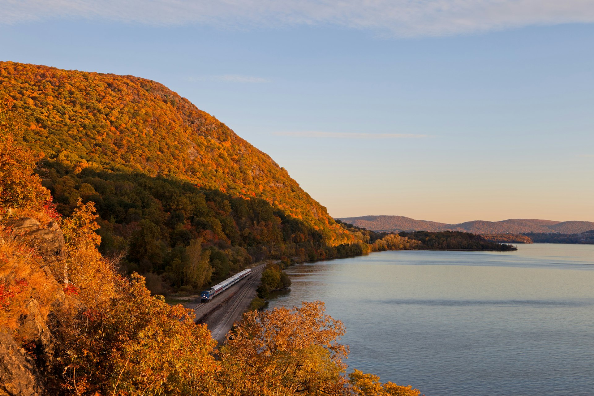 Fall foliage surrounding a NYC commuter train at sunset along the Hudson River near Cold Spring, NY