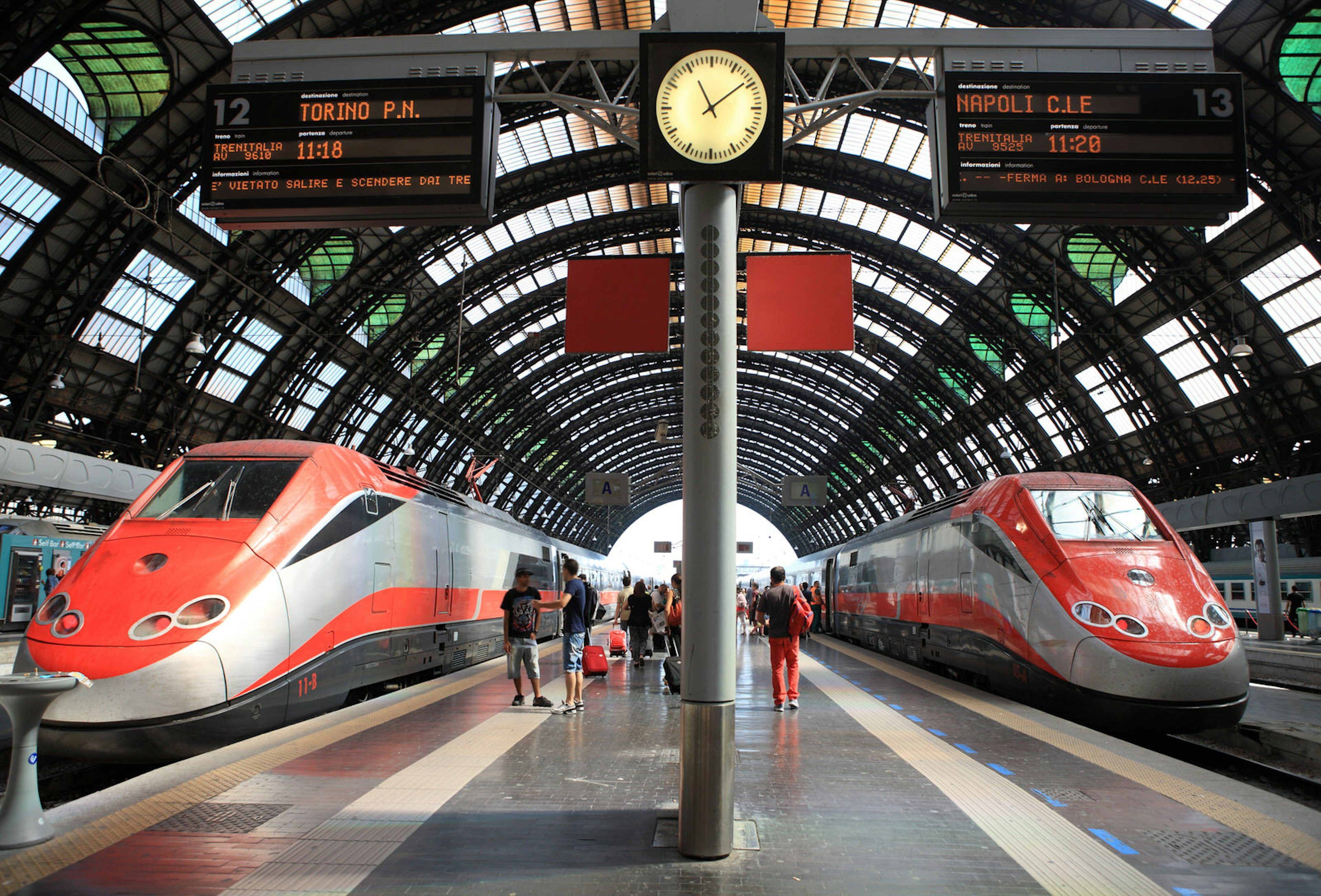 Two Frecciarossa trains await departure in a large city station with a curved glass roof