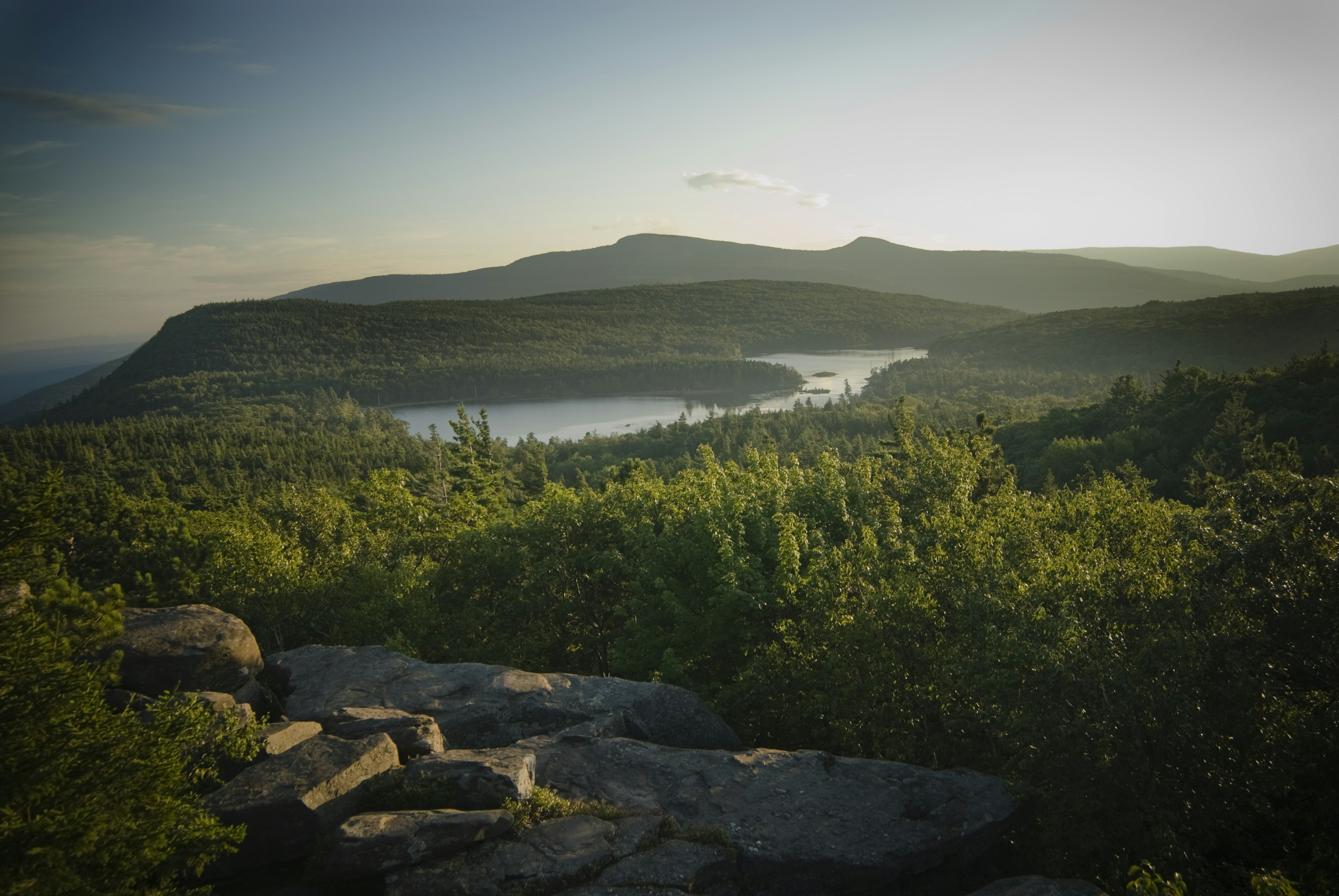 A view of the Catskills near Hunter New York, featuring green hills covered in trees, large grey boulders dappled with sunlight, and mountains in the distance