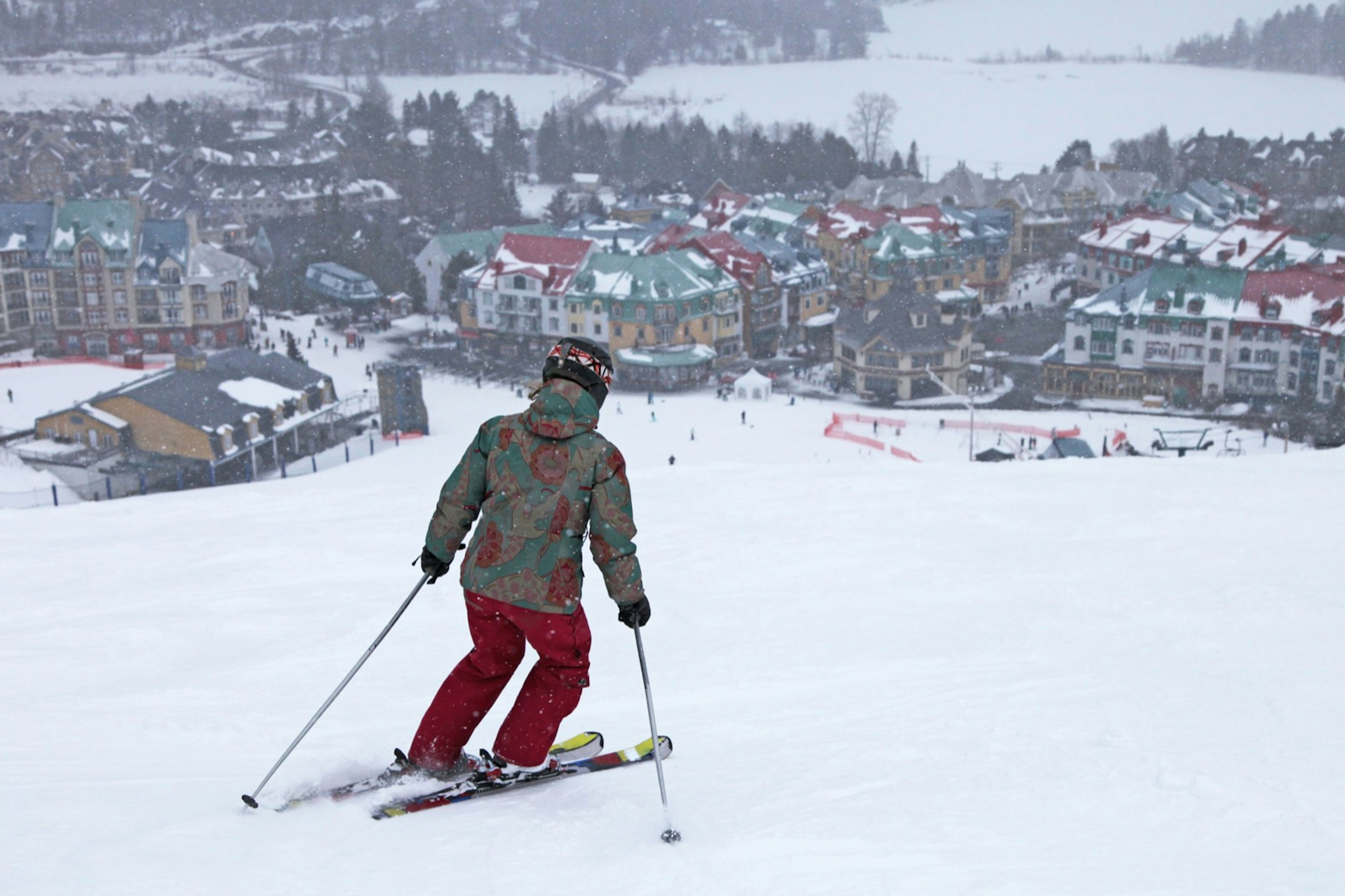 A woman skis on top of a mountain as a picturesque village, covered in snow, spreads out below her at the foot of the slope