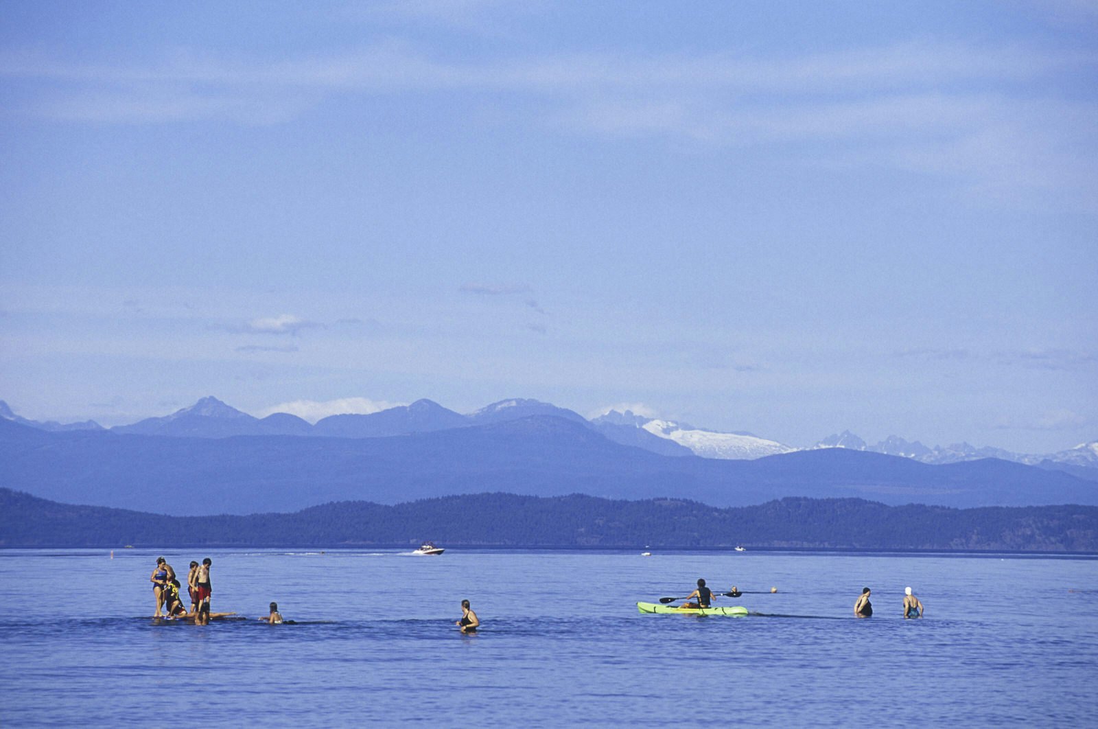 People playing in still water surrounded by mountain peaks