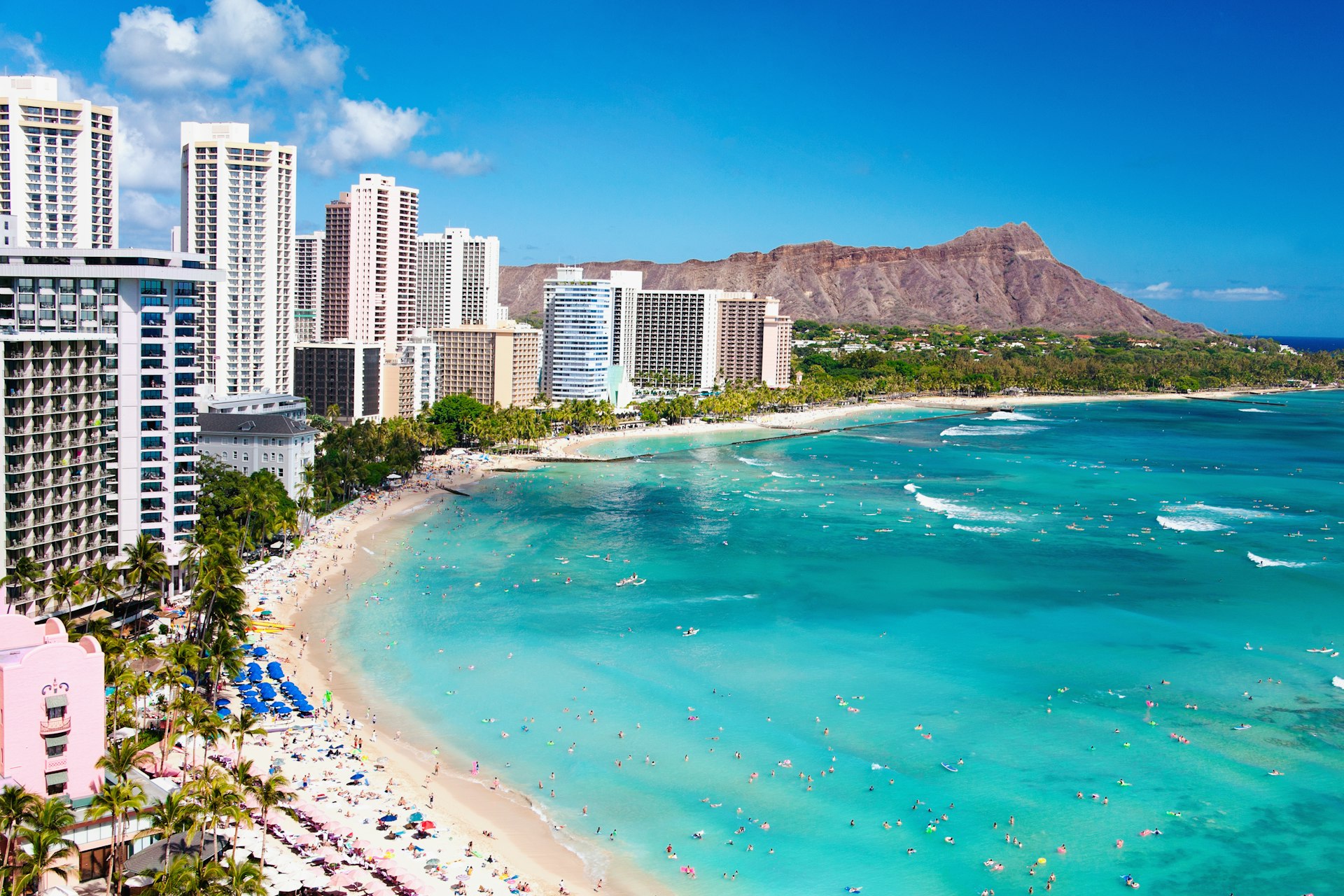 High-rise buildings hug a beach where waves crash against the shore