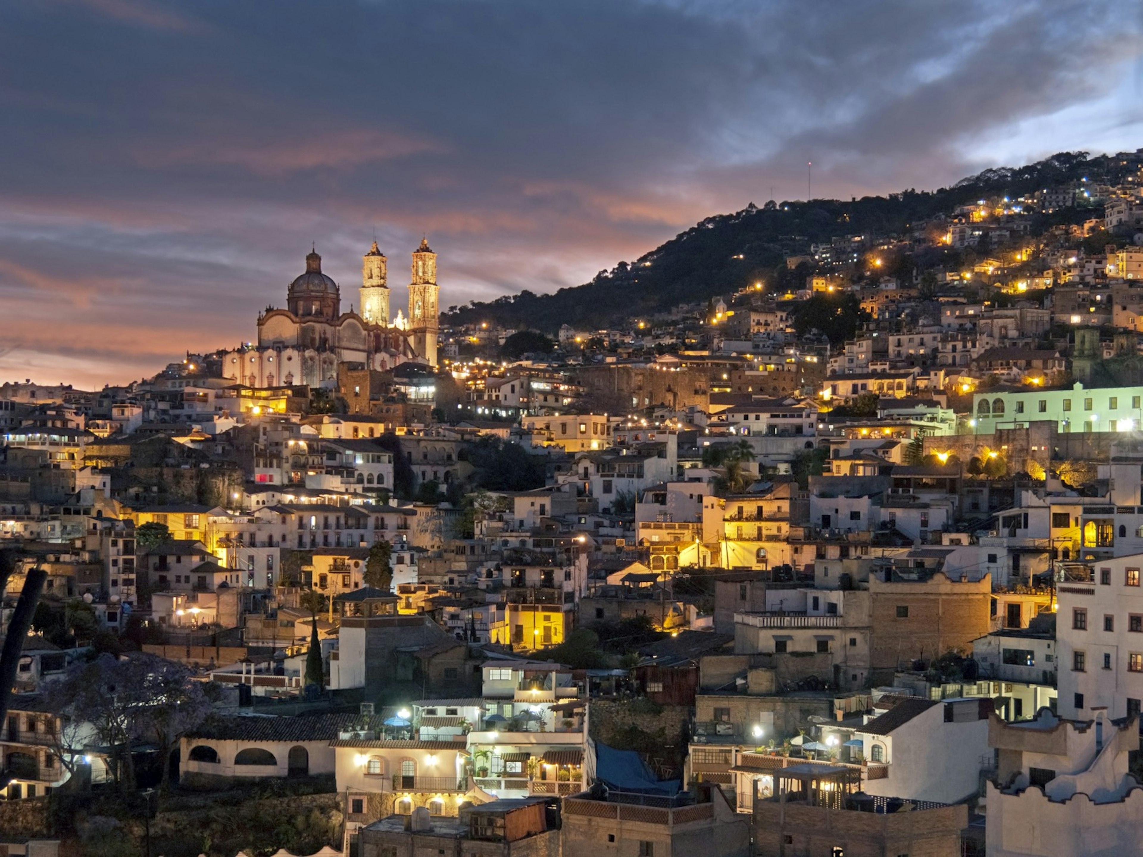 White buildings with red roofs built densely together crawl up a mountain in Taxco, Mexico.