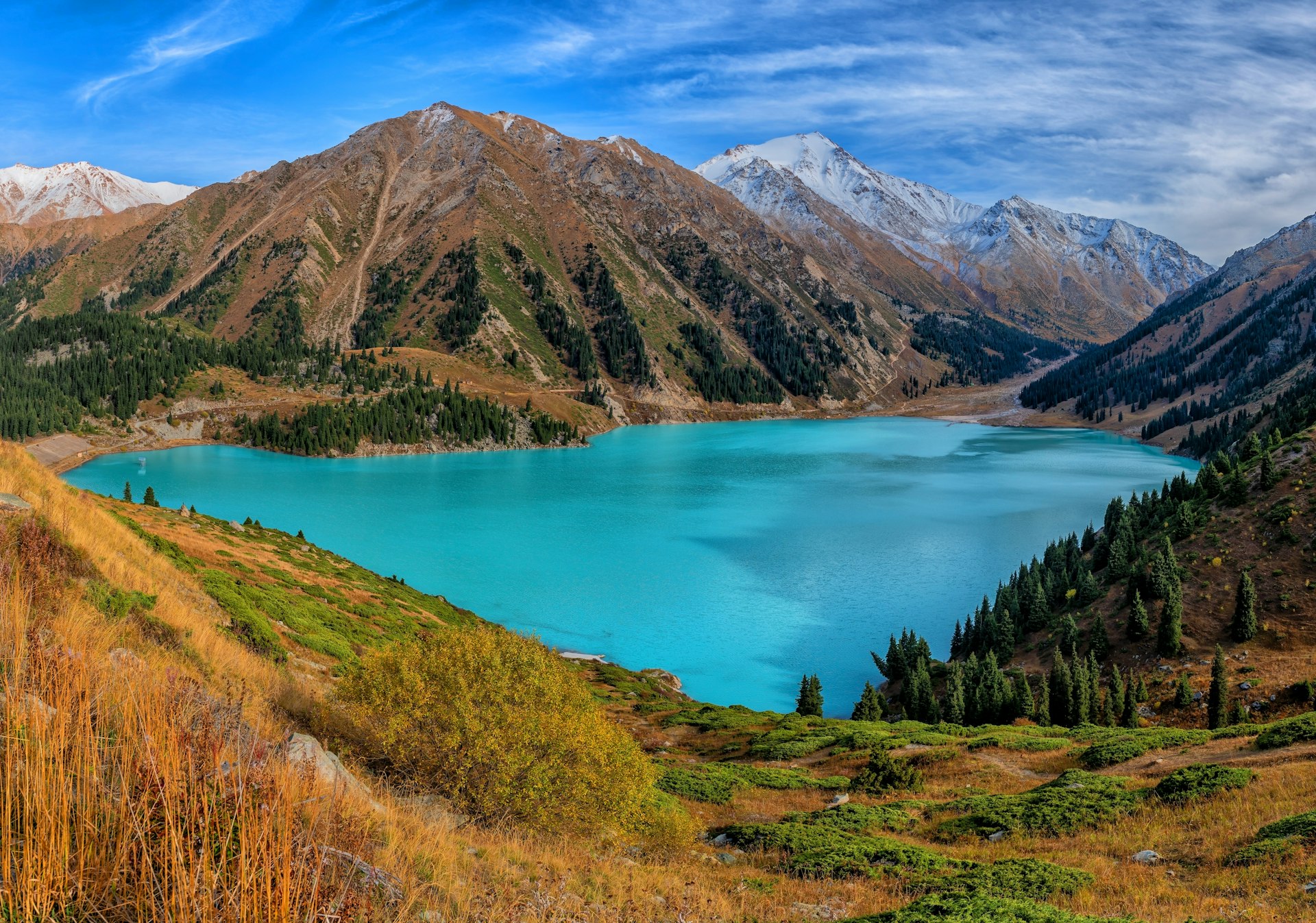 A large turquoise lake framed by green mountains with snow on the highest peaks