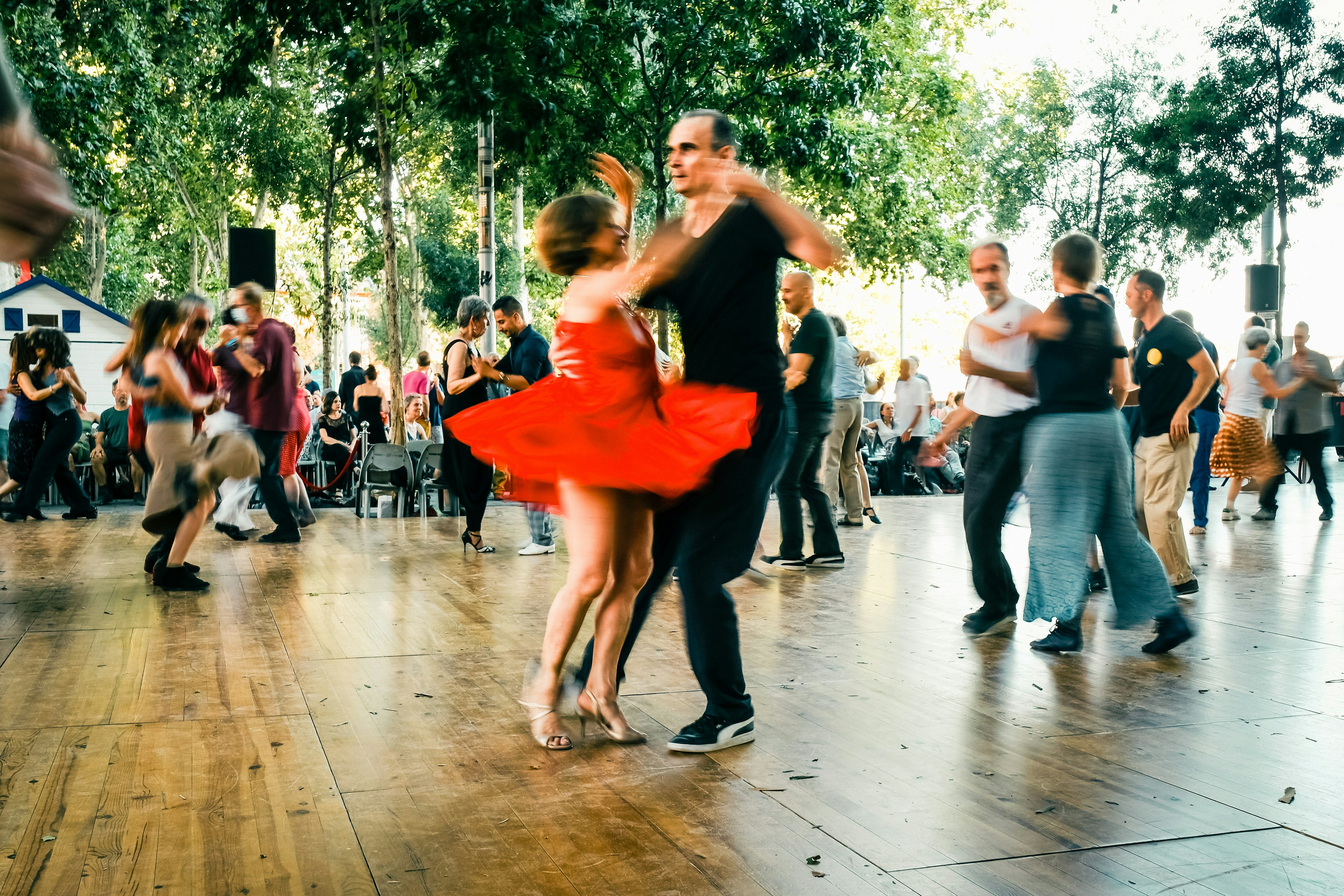 A couple in motion, including a woman in a read dress, dances in a public square as part of the Tangopostale festival, Toulouse, France