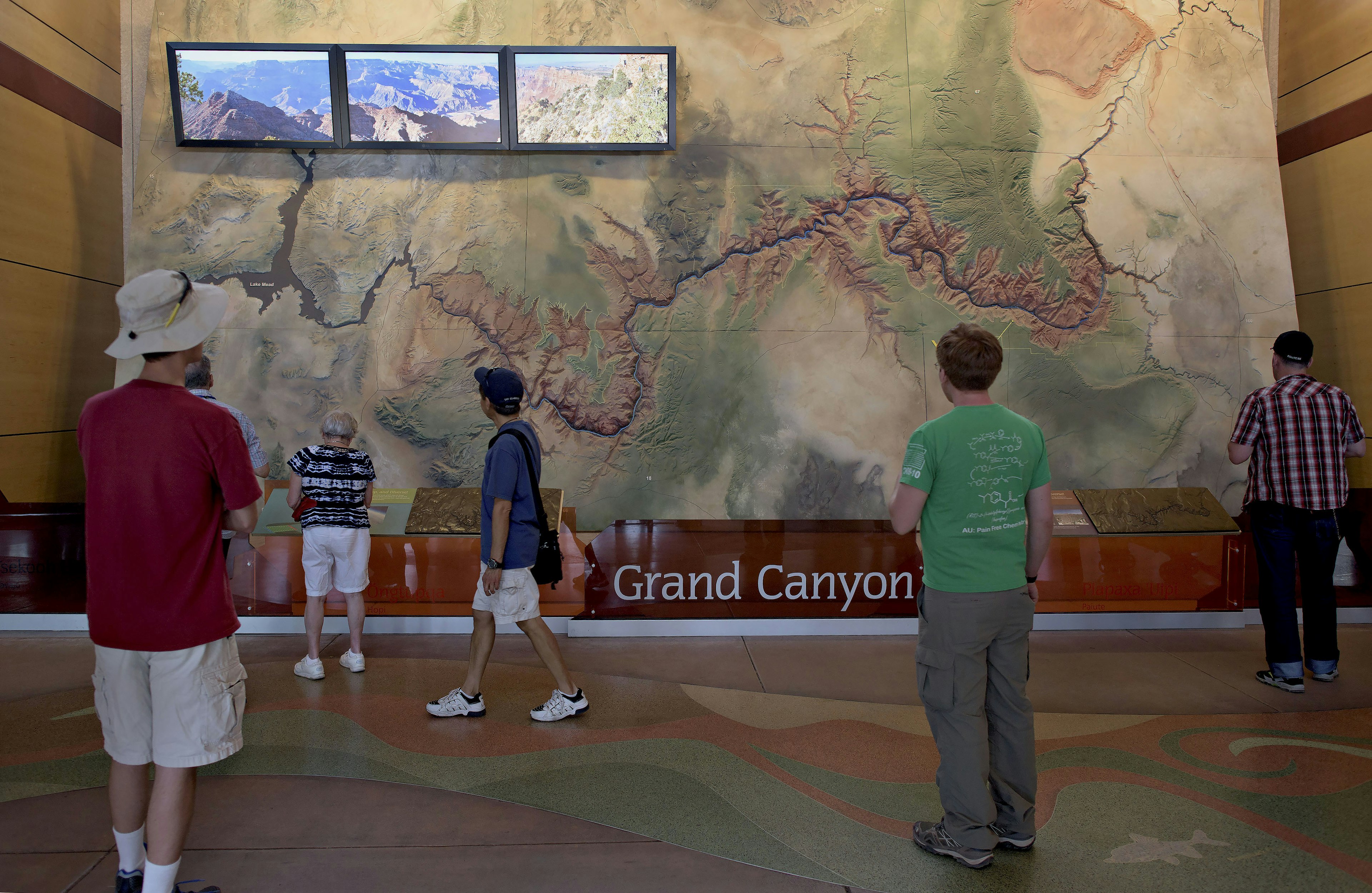 Six tourists stand in front of a large, wall-sized topographic map of the Grand Canyon