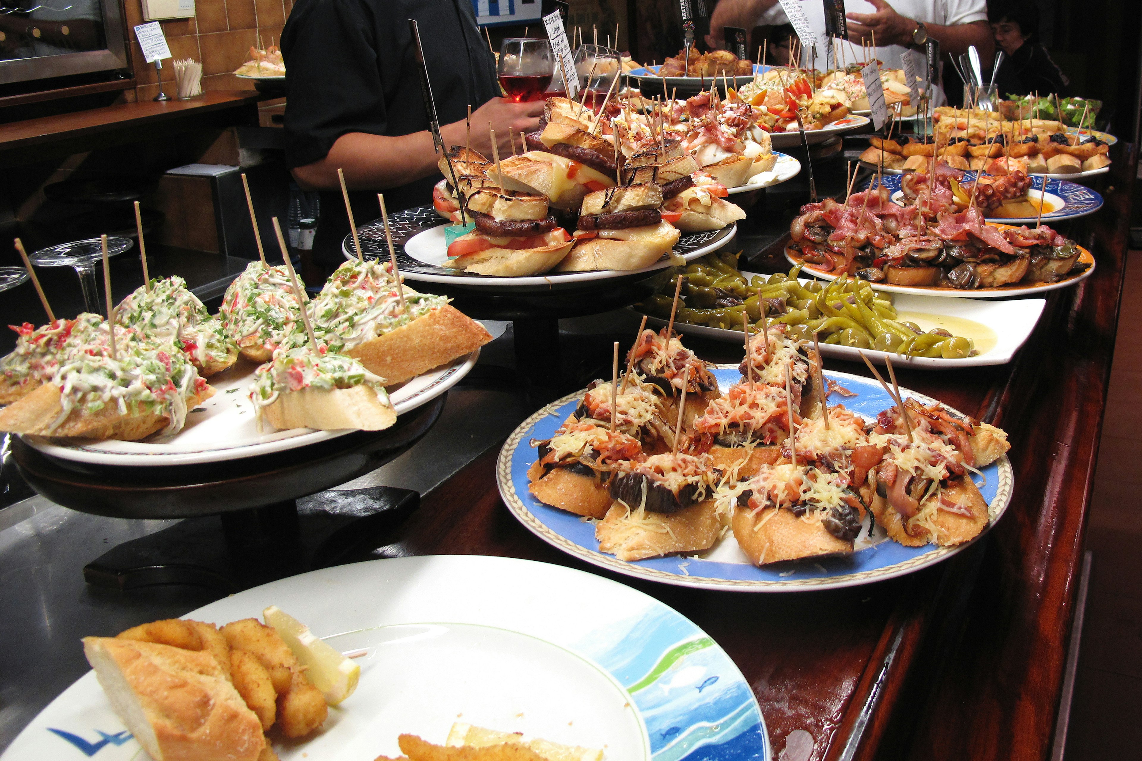 A table filled with a large spread of sandwiches, peppers and bread; visit Basque country