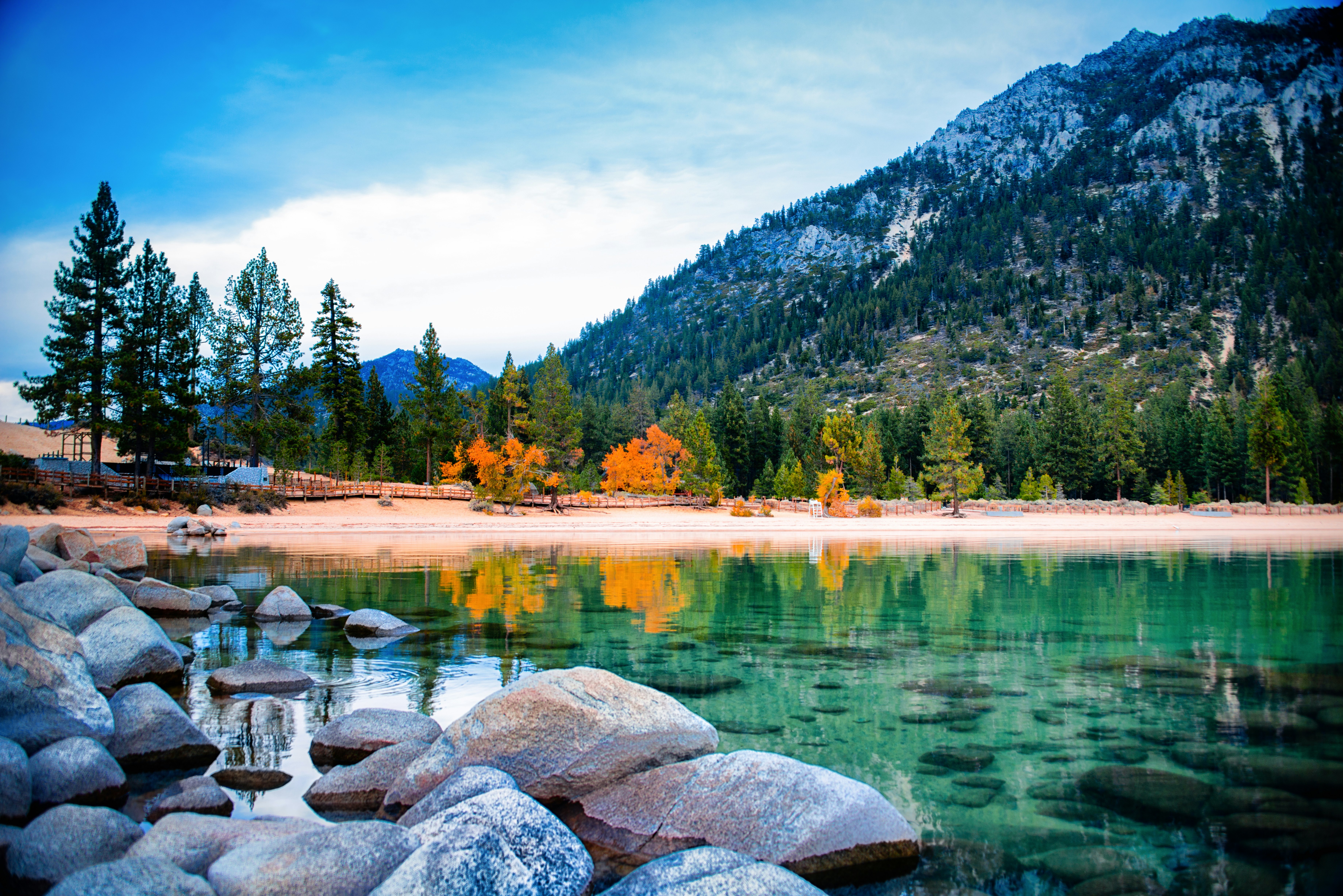 A lake near a mountain, with an empty beach and fall colors on the trees