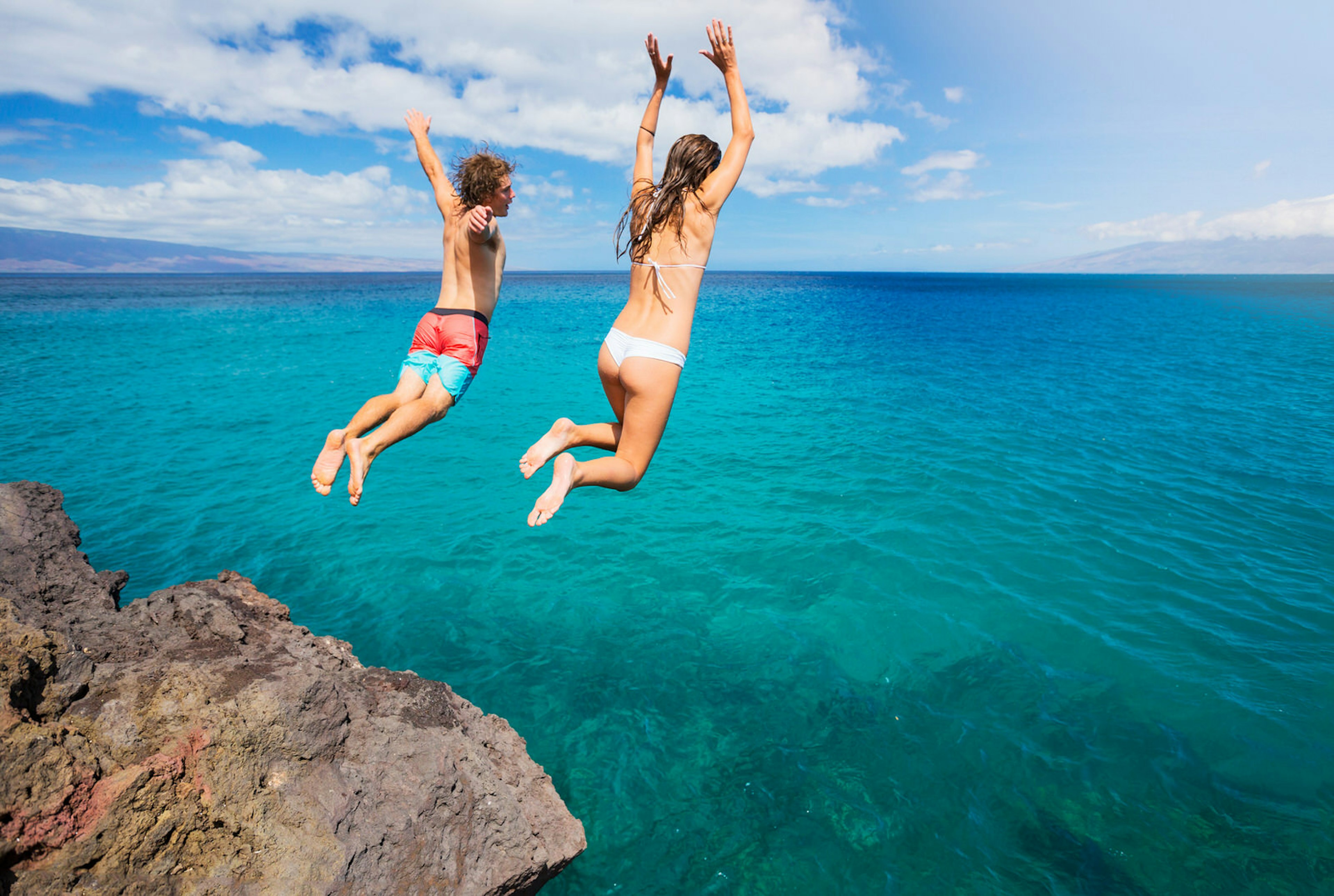 A man and woman cliff jumping into the turquoise ocean © EpicStockMedia / Getty Images