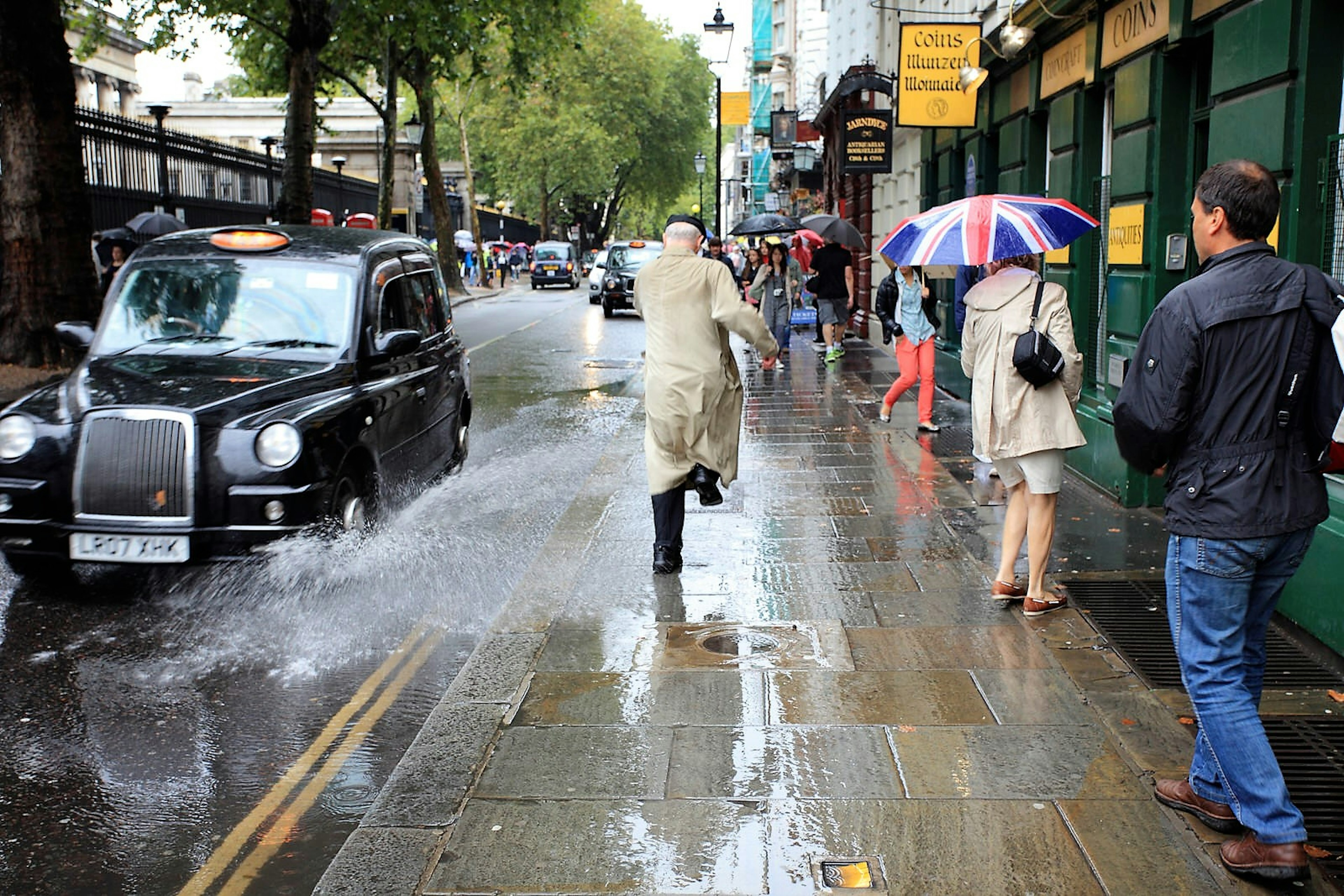 Man getting splashed by a taxi in the rain.