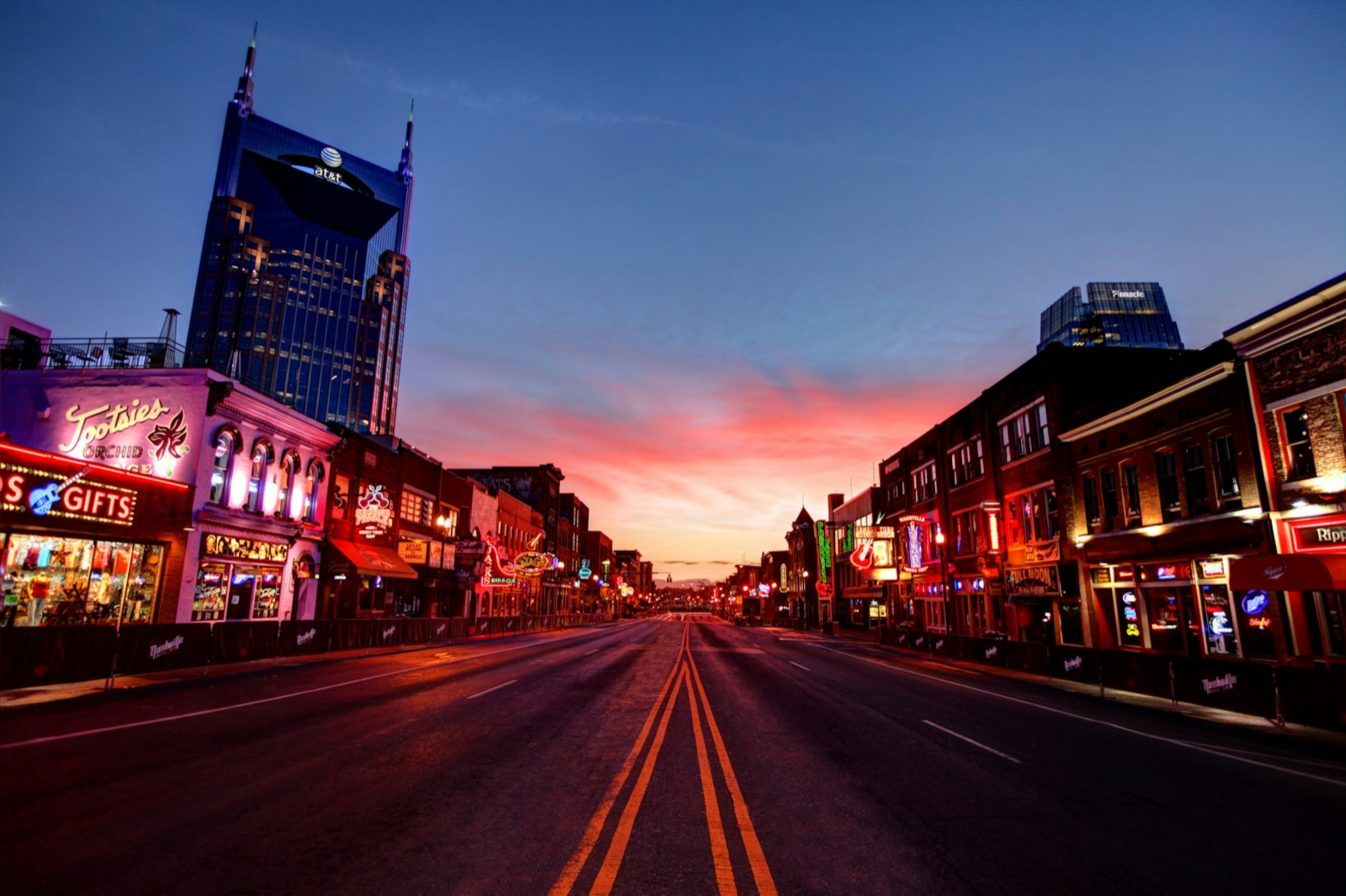 A road at sunset lined with lit up buildings with neon signs. Southern Lady Code is an excellent audiobooks for US Road trip selection.