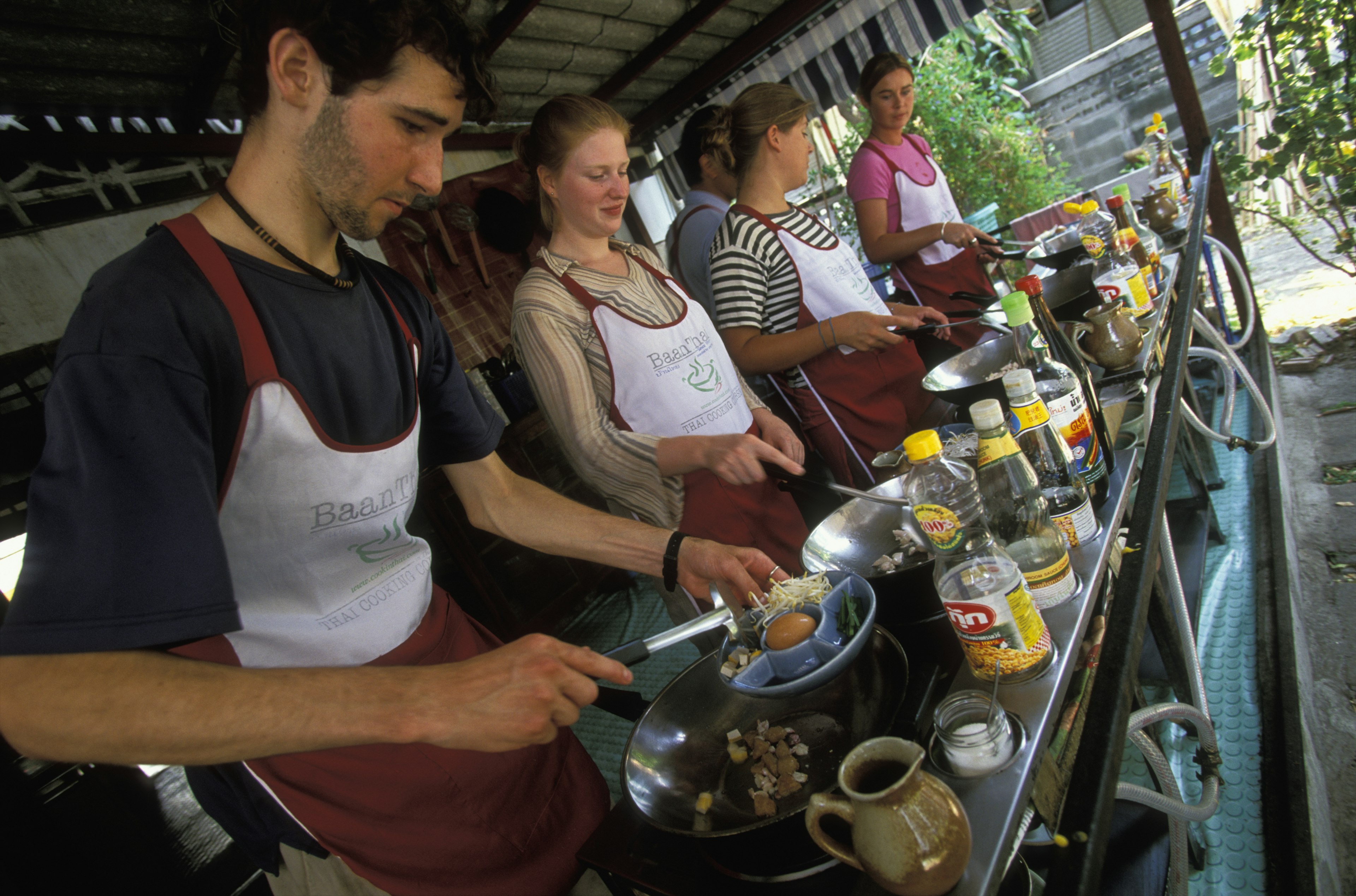 a line of people wearing aprons have woks and food in front of them