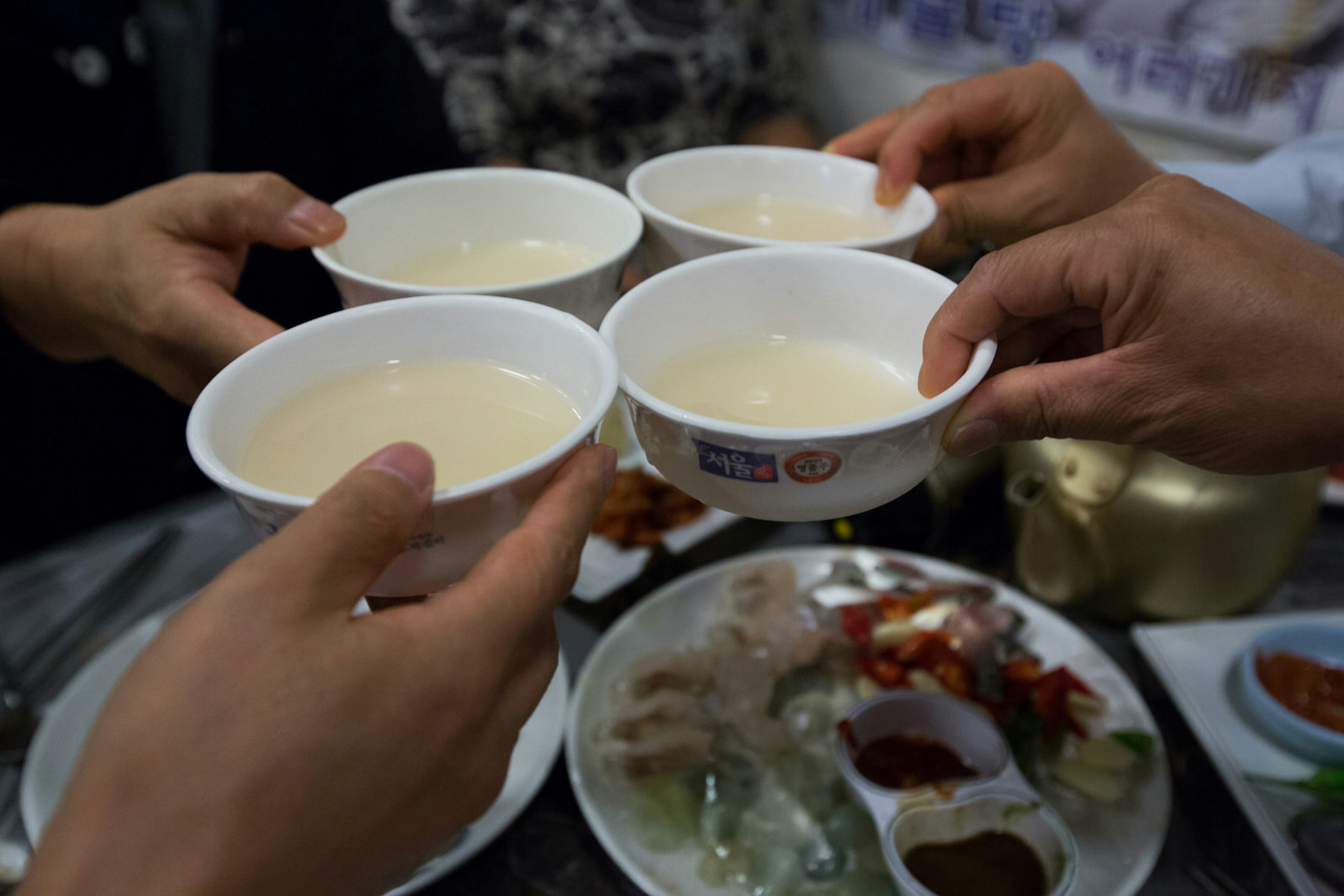 People sharing a toast bowls of makgeolli, Korean rice wine.