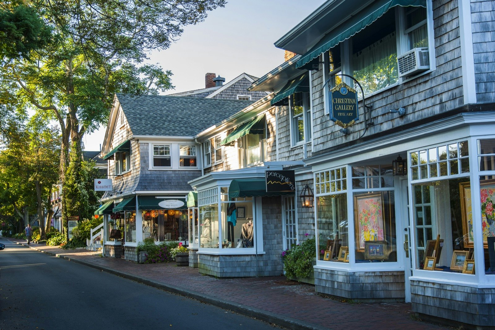 An empty street lined with buildings all with grey cedar shake siding and white trimmed windows.