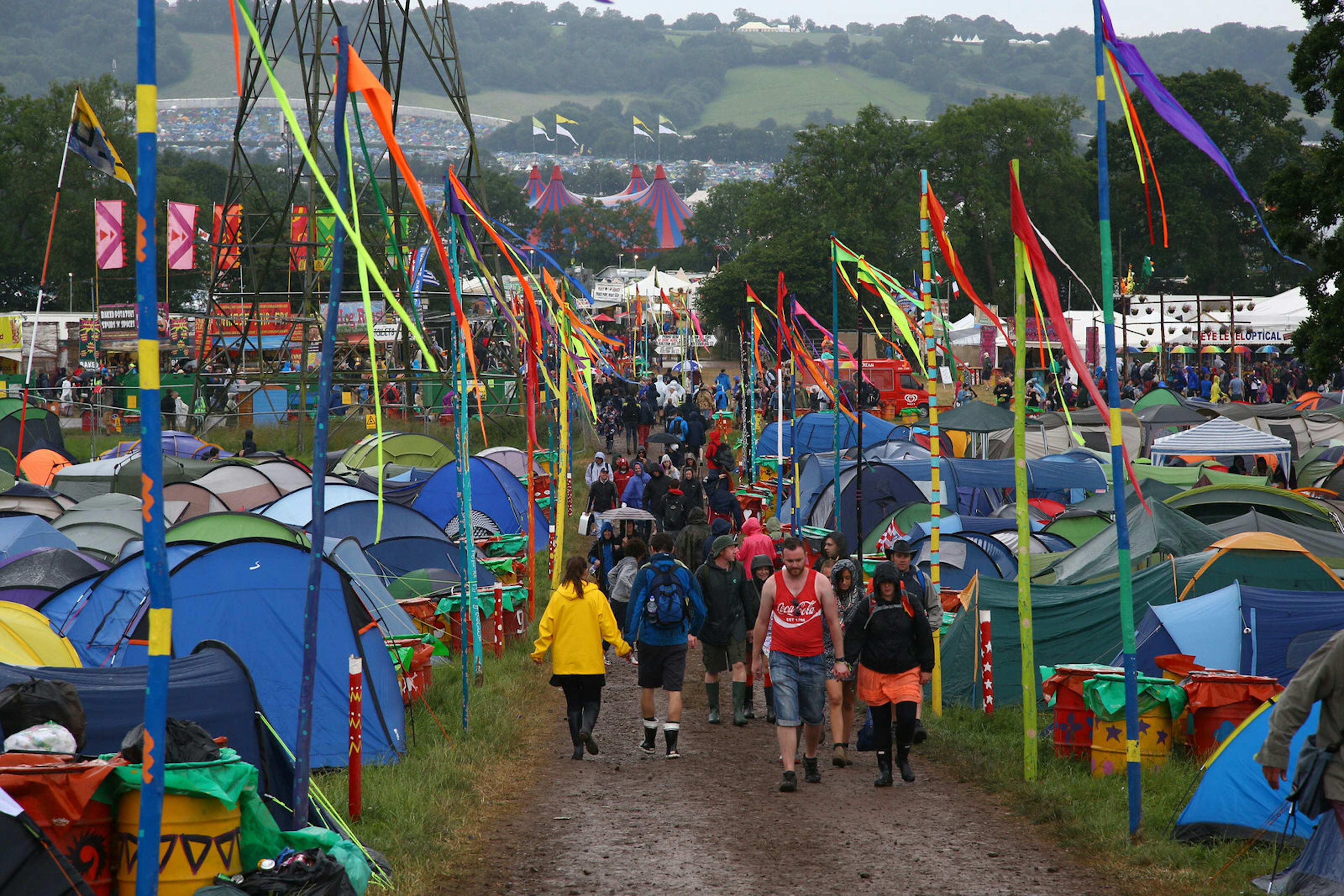 Festival goers trudge down a muddy path between tents at a campsite