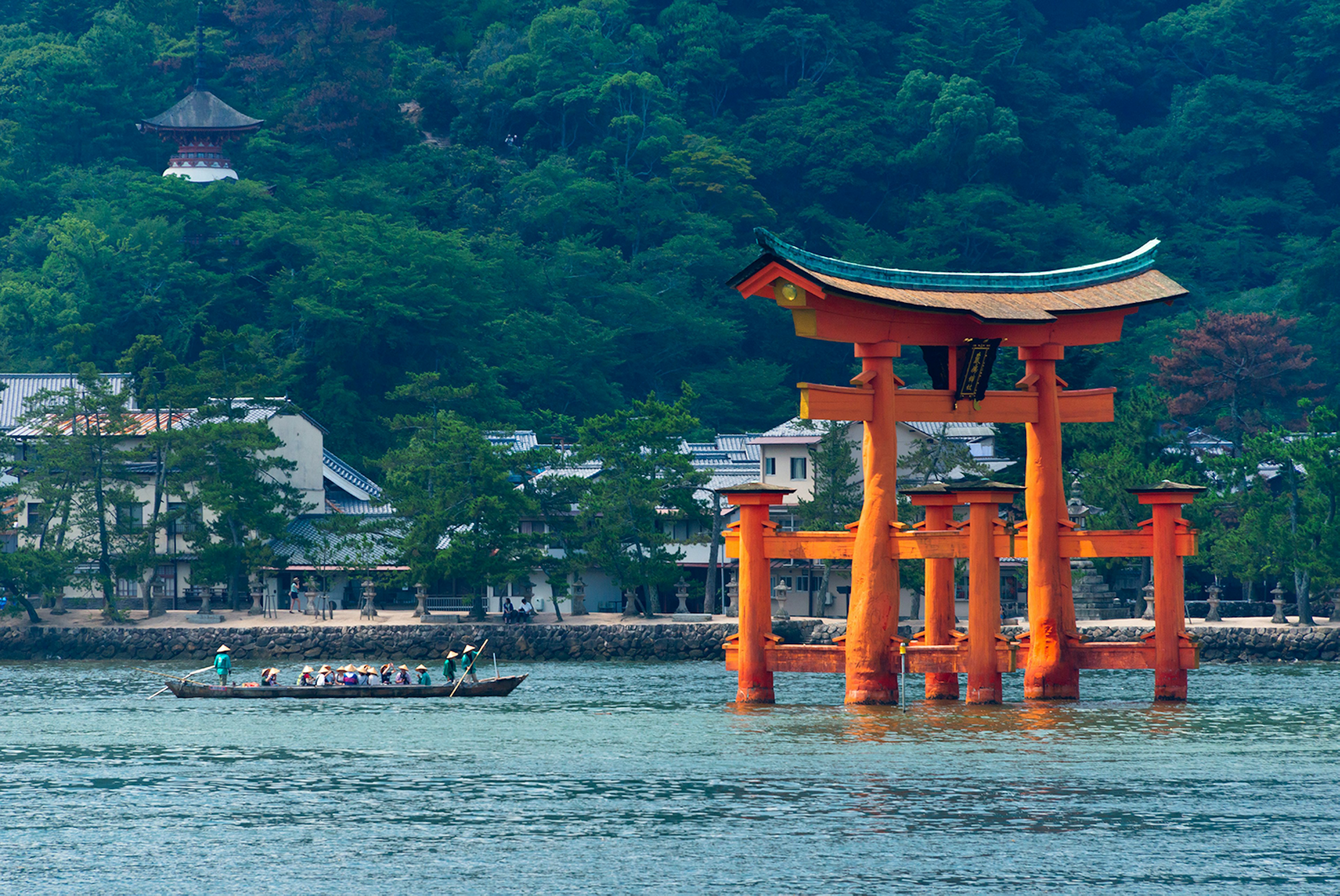 A row boat with 16 rowers approaching a Japanese torii gate, which stands in water; best things to do in the summer in Japan