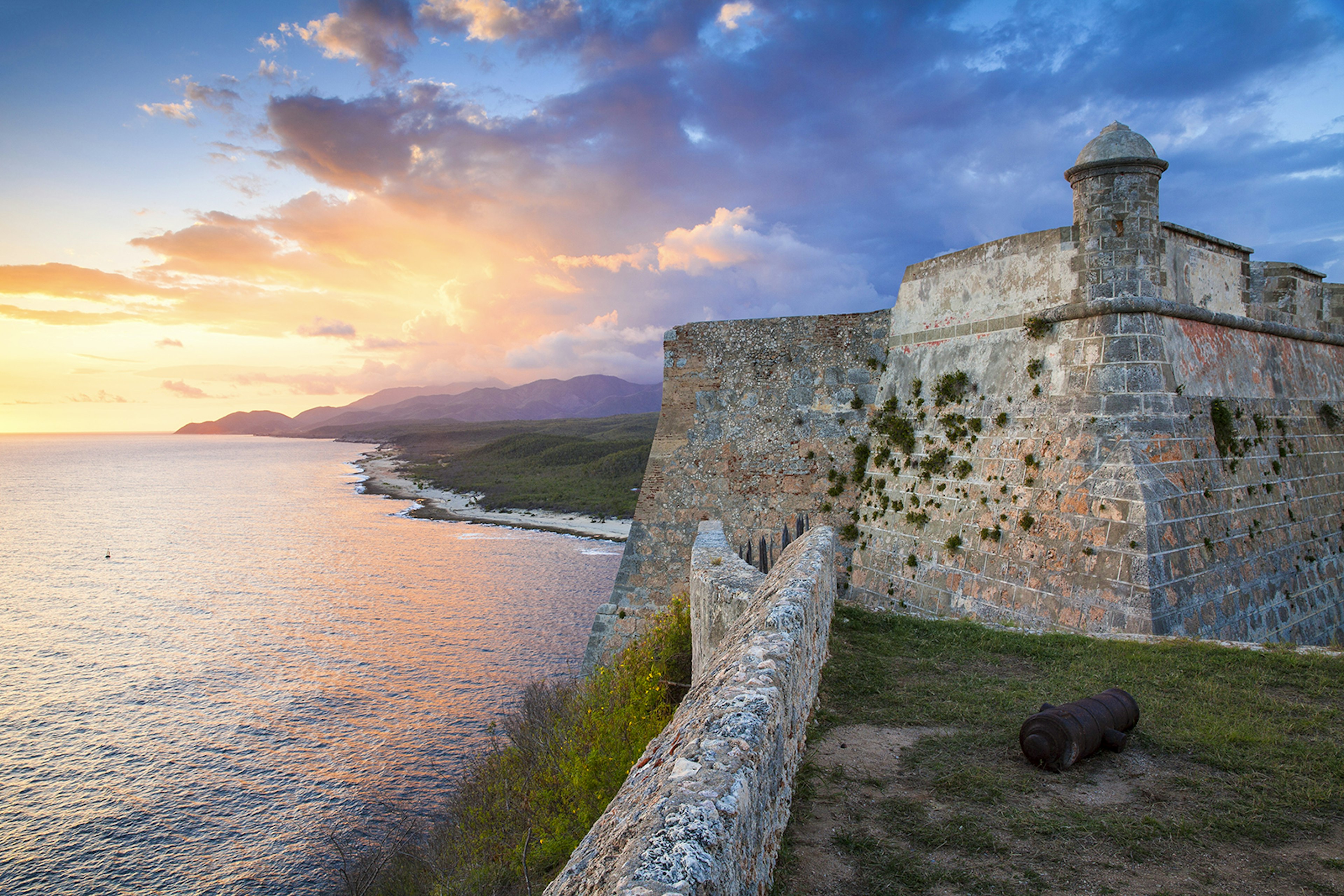 Cuba, Santiago de Cuba Province, Santiago de Cuba, Lighthouse at Castillo de San Pedro de la Roca del Morro (Castillo del Morro)  - Now home to the Museo de la Piratería – Pirate museum
528822791
no people, horizontal, outdoors, sunset, sunlight, cloud, architecture, unesco world heritage site, castle, mountain range, sea, lighthouse, travel destinations, fort, castillo del morro, castillo de san pedro de la roca del morro, citadel, cuba, museum, santiago de cuba, santiago de cuba province, lawn, grass, stone wall, remote