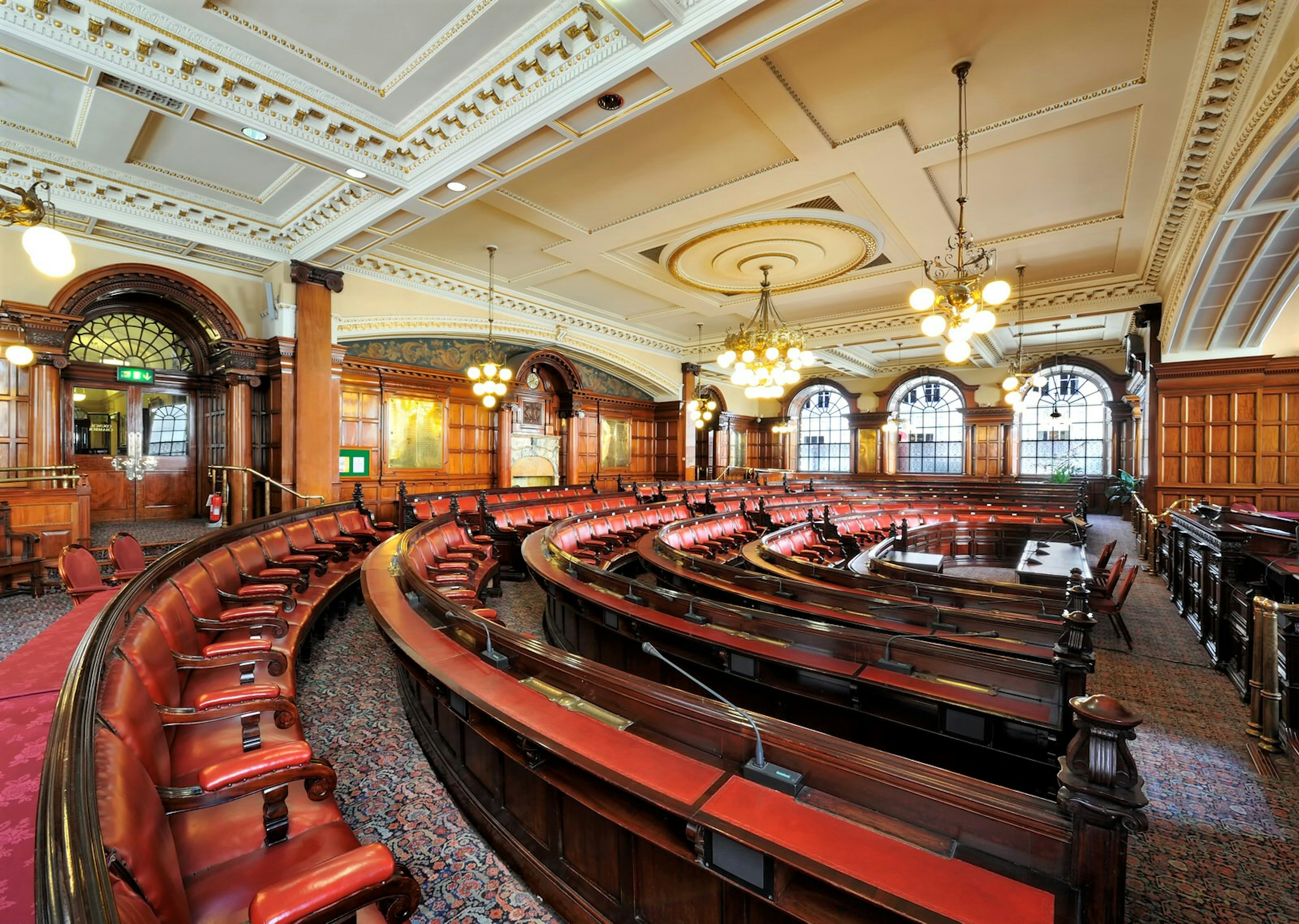 Liverpool Town Hall interior complete with curved rows of red leather seats, dark wood panelled walls and chandeliers