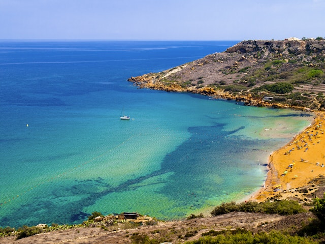 A beach with terracotta-colored sand and pale, light-blue waters