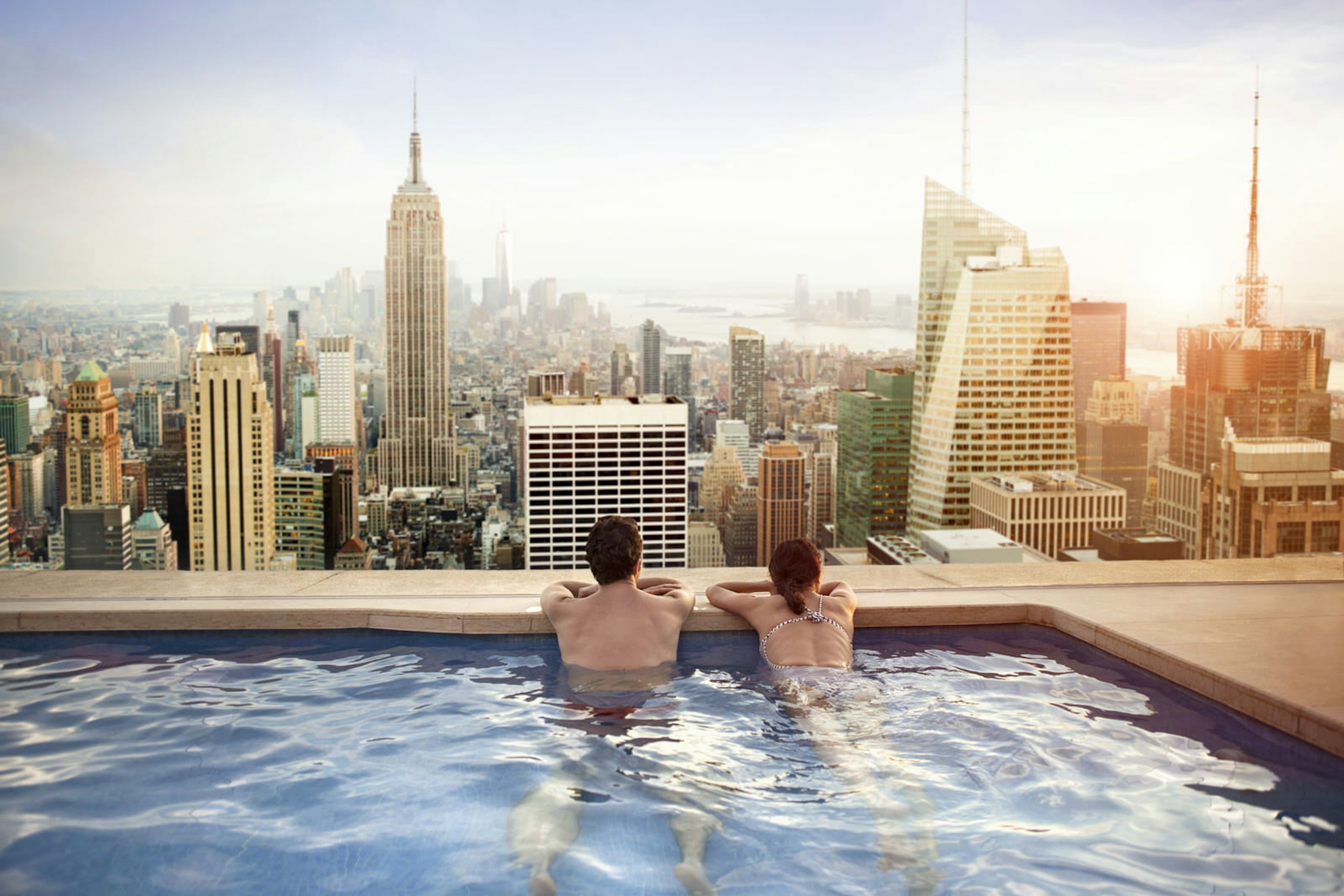 A couple in a rooftop pool staring out at the Manhattan skyline