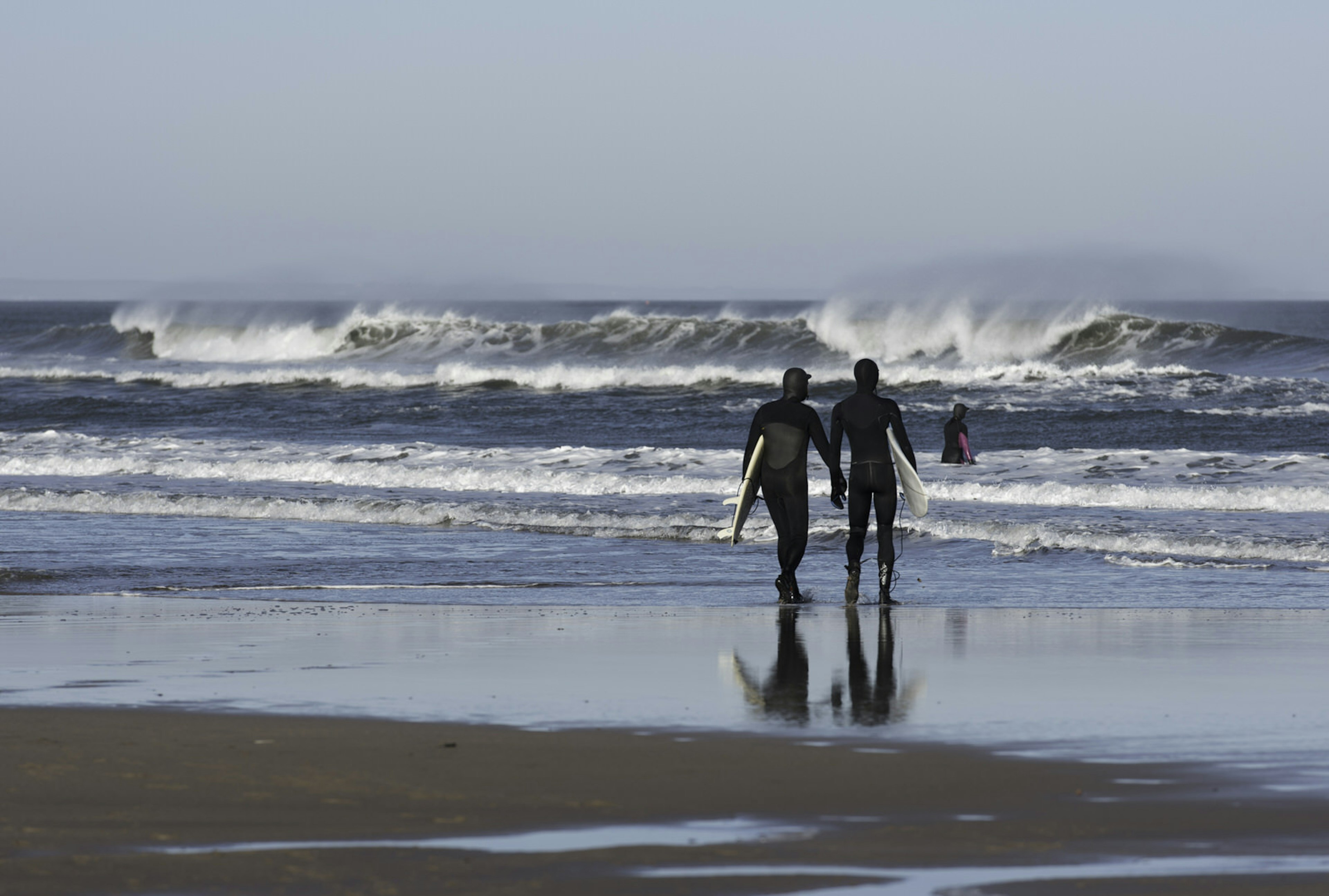 Two surfers walk to the water at Belhaven Bay