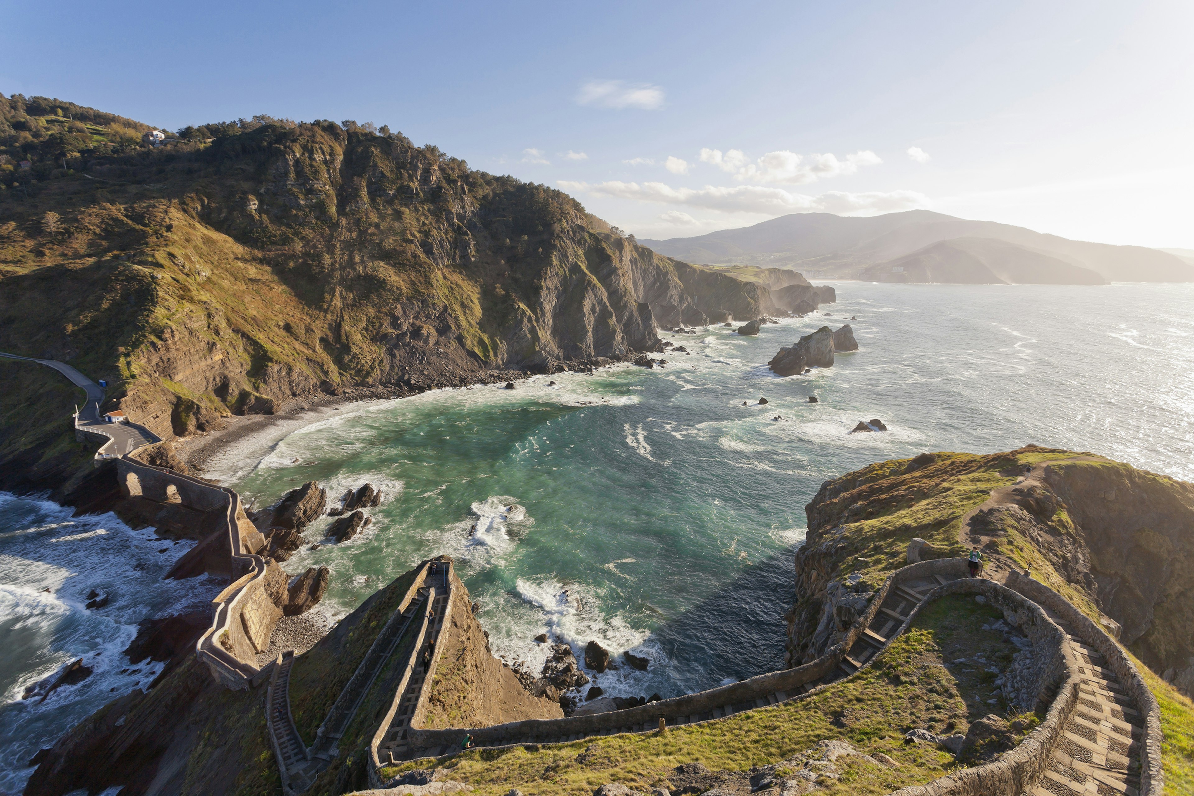 Winding stone steps run along the top of high grassy hills next to the ocean; visit Basque Country