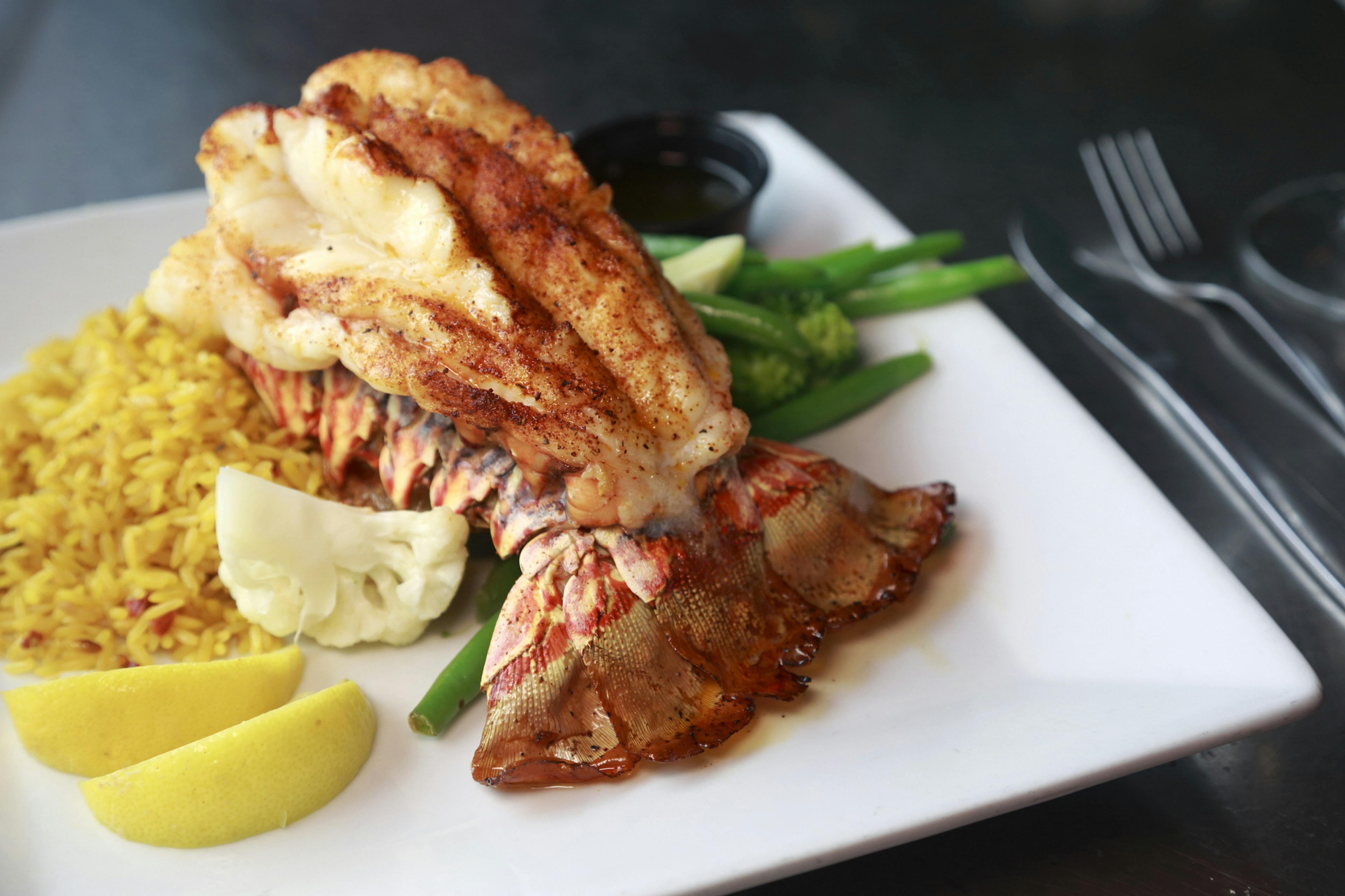 Lobster tail served on a white plate on a bed of green beans and yellow rice