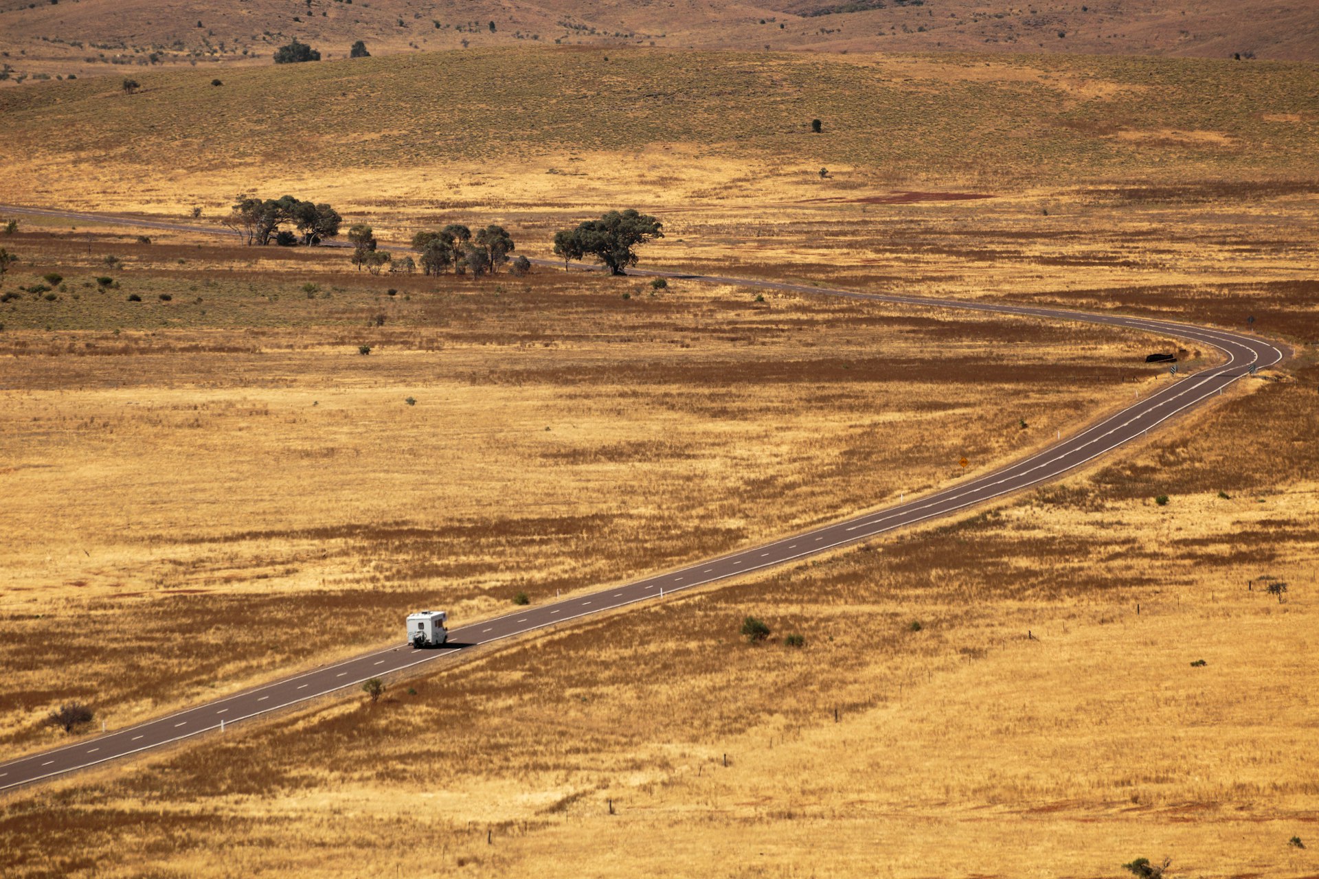 A motor home drives along a long open road through an empty vast landscape