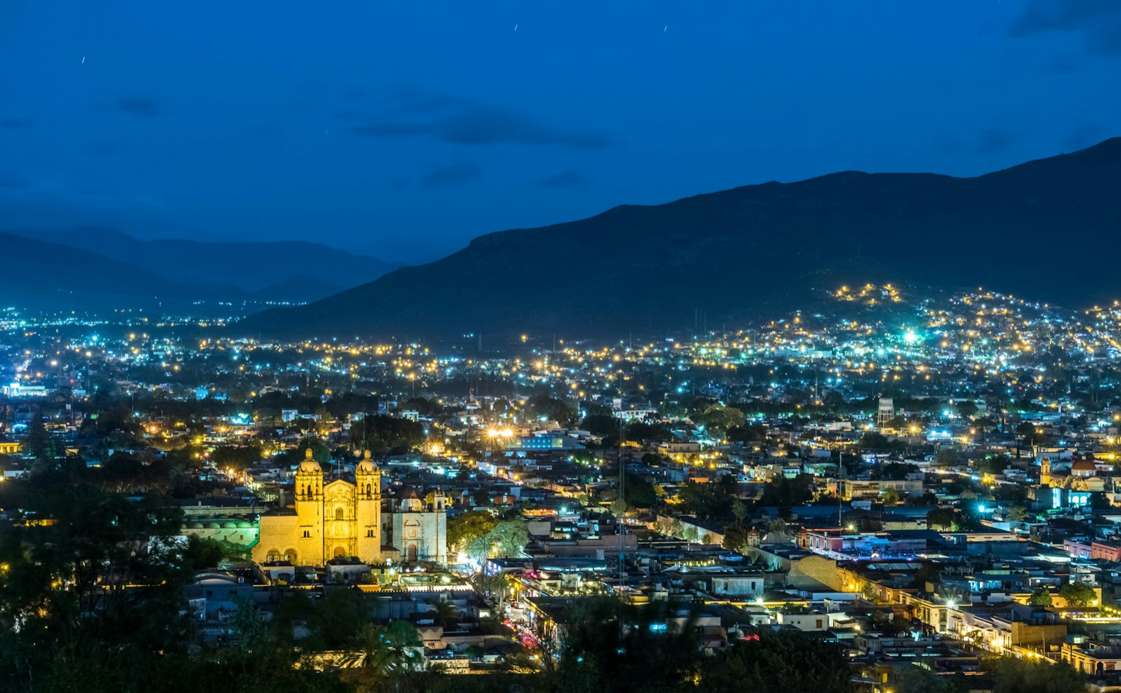 City lights stretch to a mountain in the horizon with a cathedral in the middle bathed in bright gold light