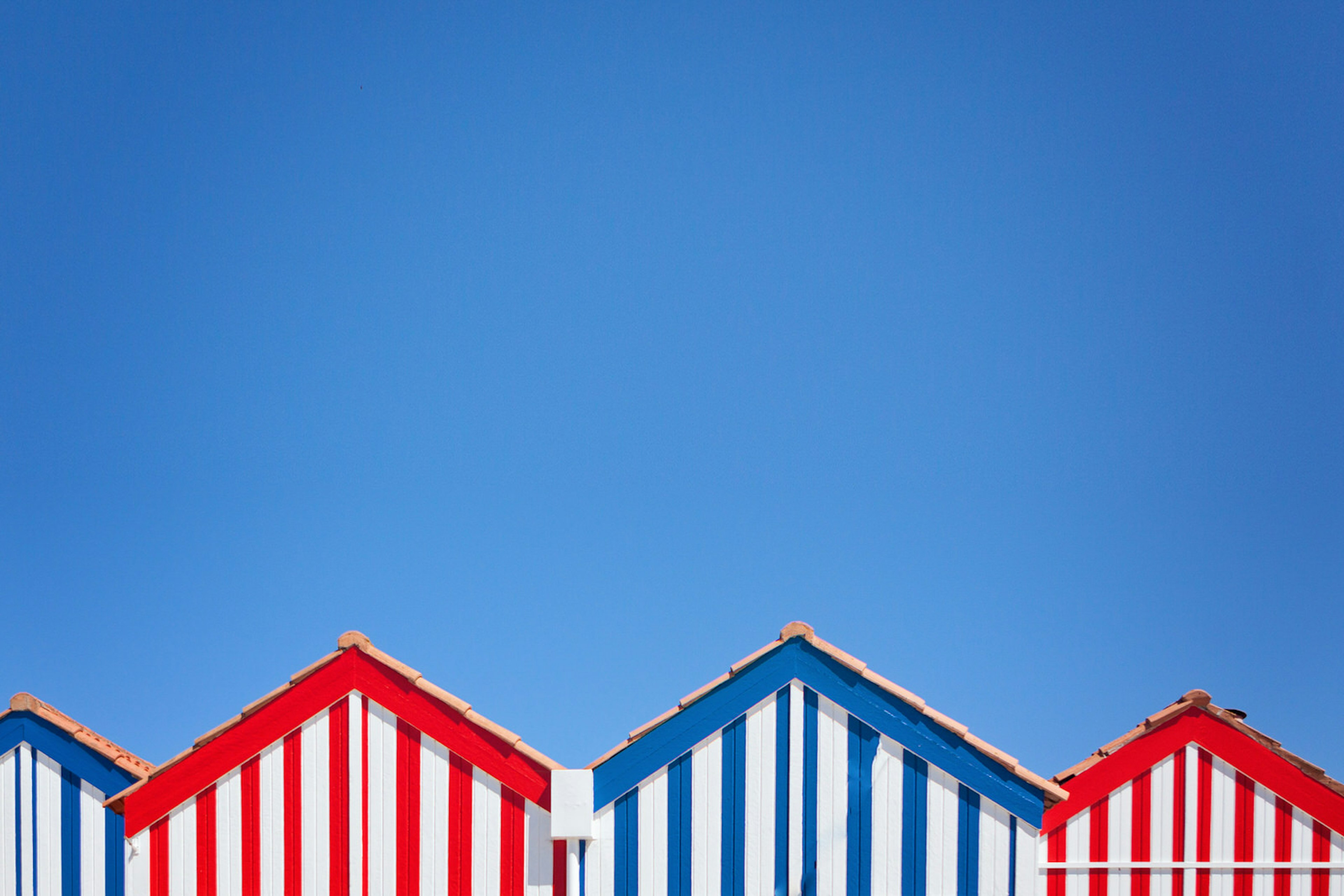 Red, white and blue stripy beach huts in Costa Nova, Portugal © Carol Yepes / Getty Images