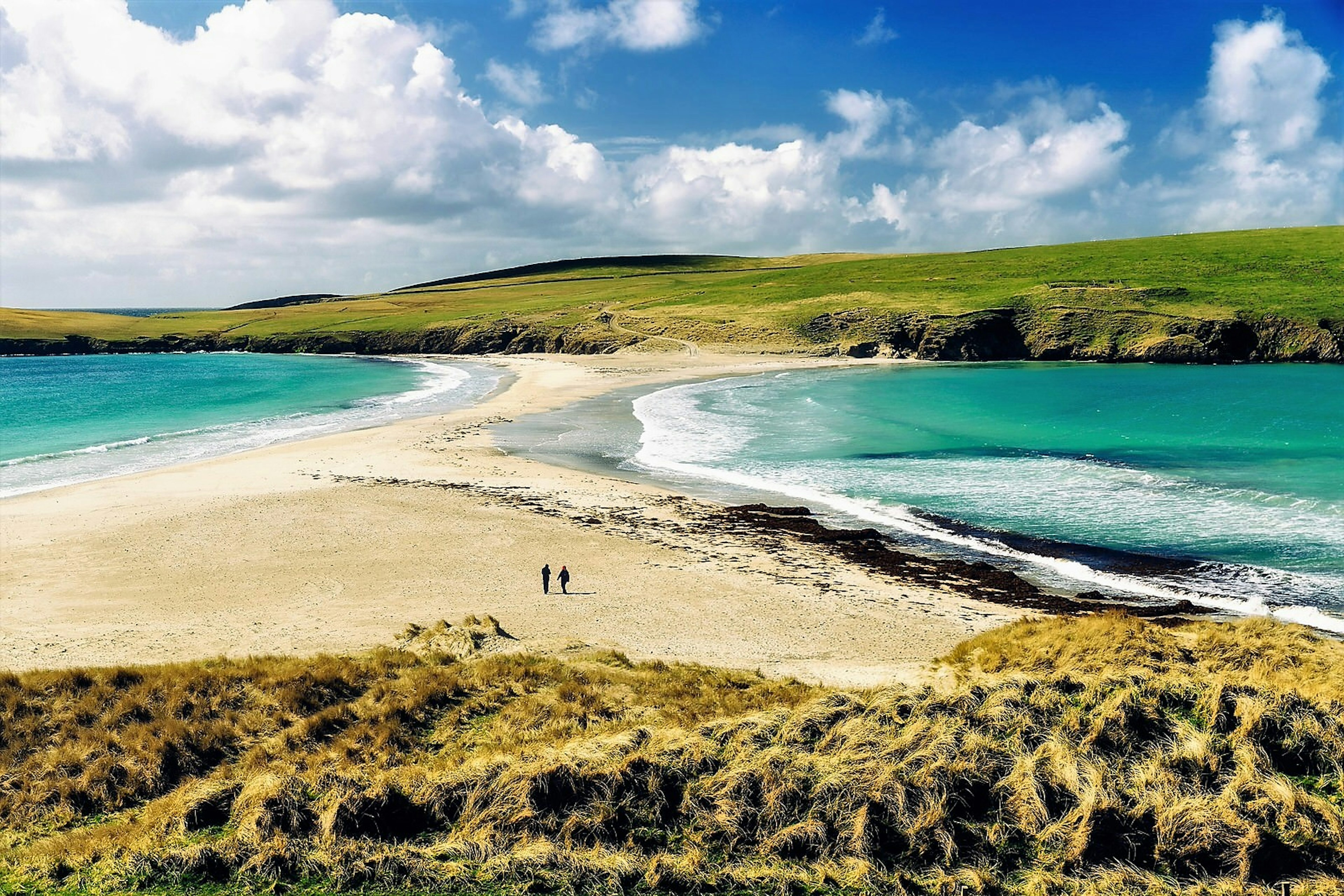 A couple walk across an empty beach in Shetland