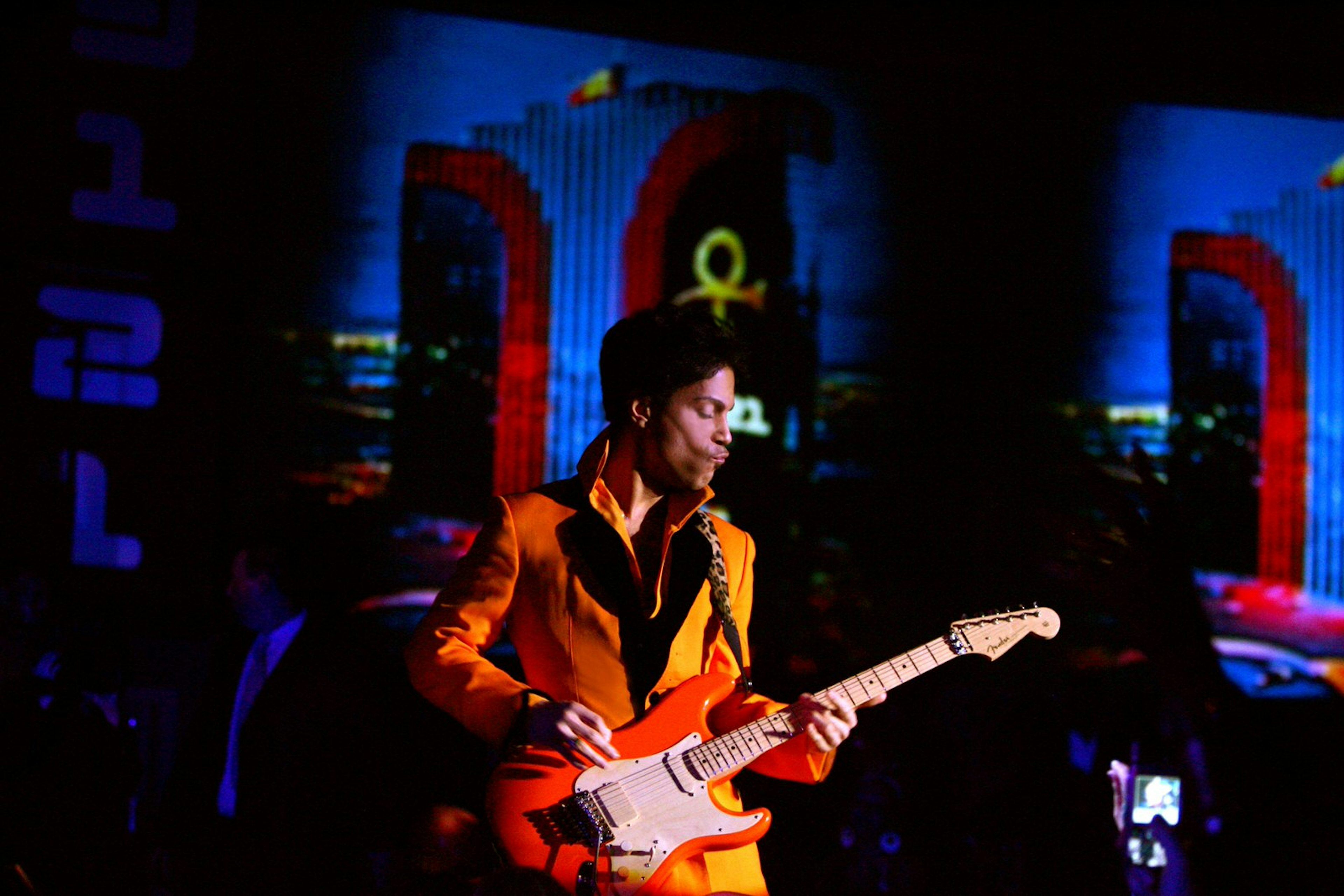 Prince performing at the Rio Hotel in Las Vegas, dressed in a flamboyant orange jacket and playing a matching orange electric guitar