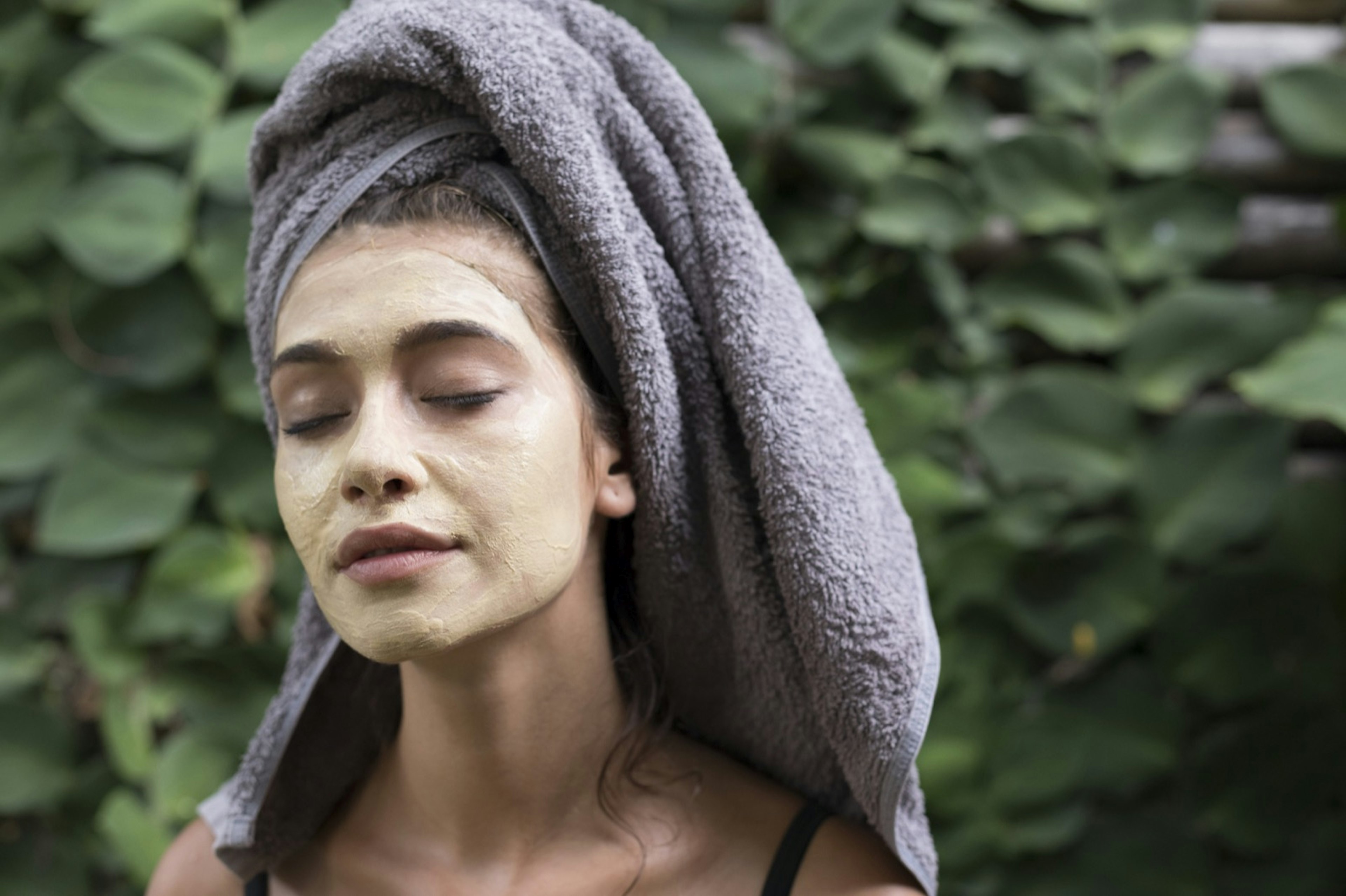 A woman wears a grey towel on her head with a yellow face mask; her eyes are closed as she creates a sacred space