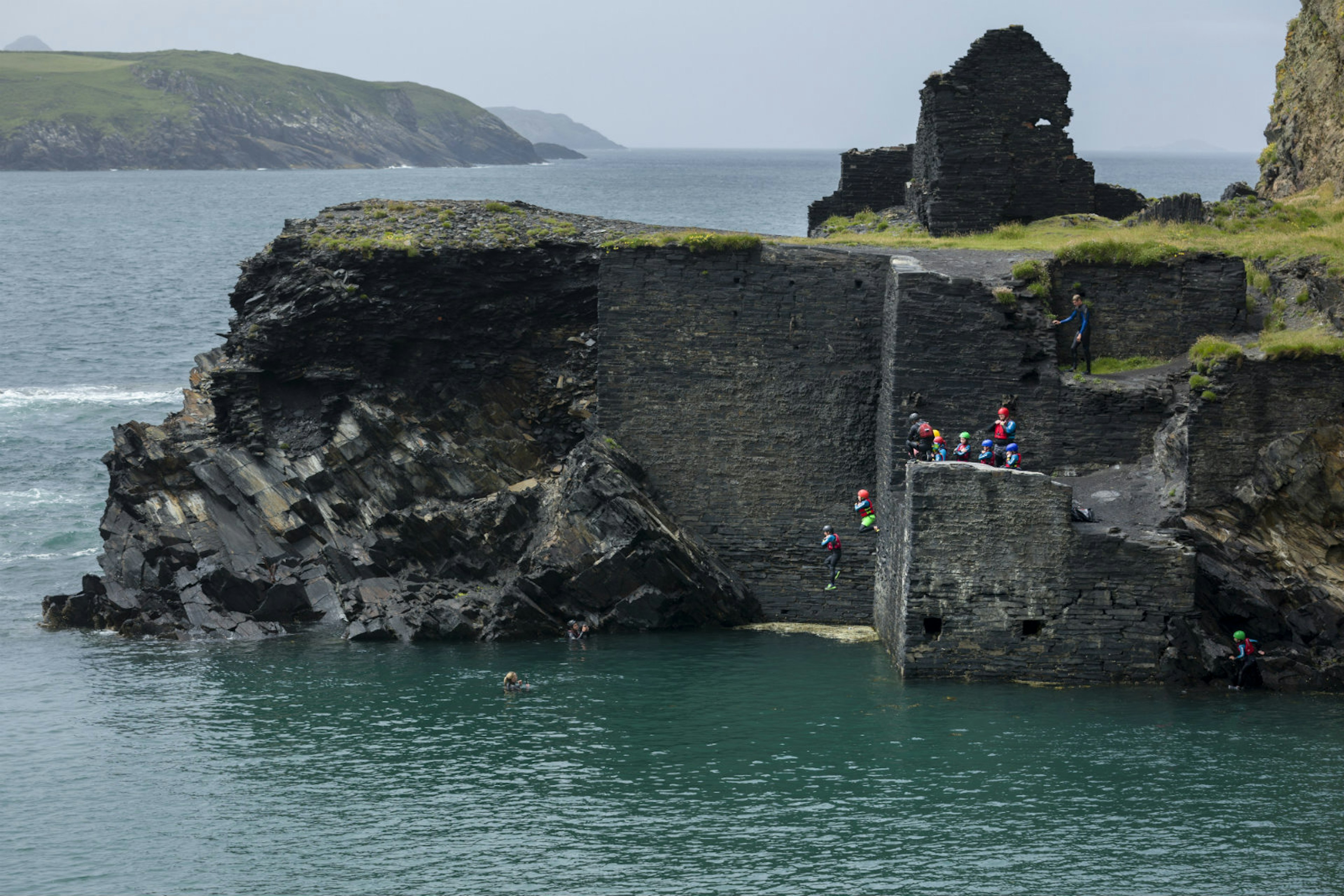 A coasteering group jump into the sea off the coast of Wales