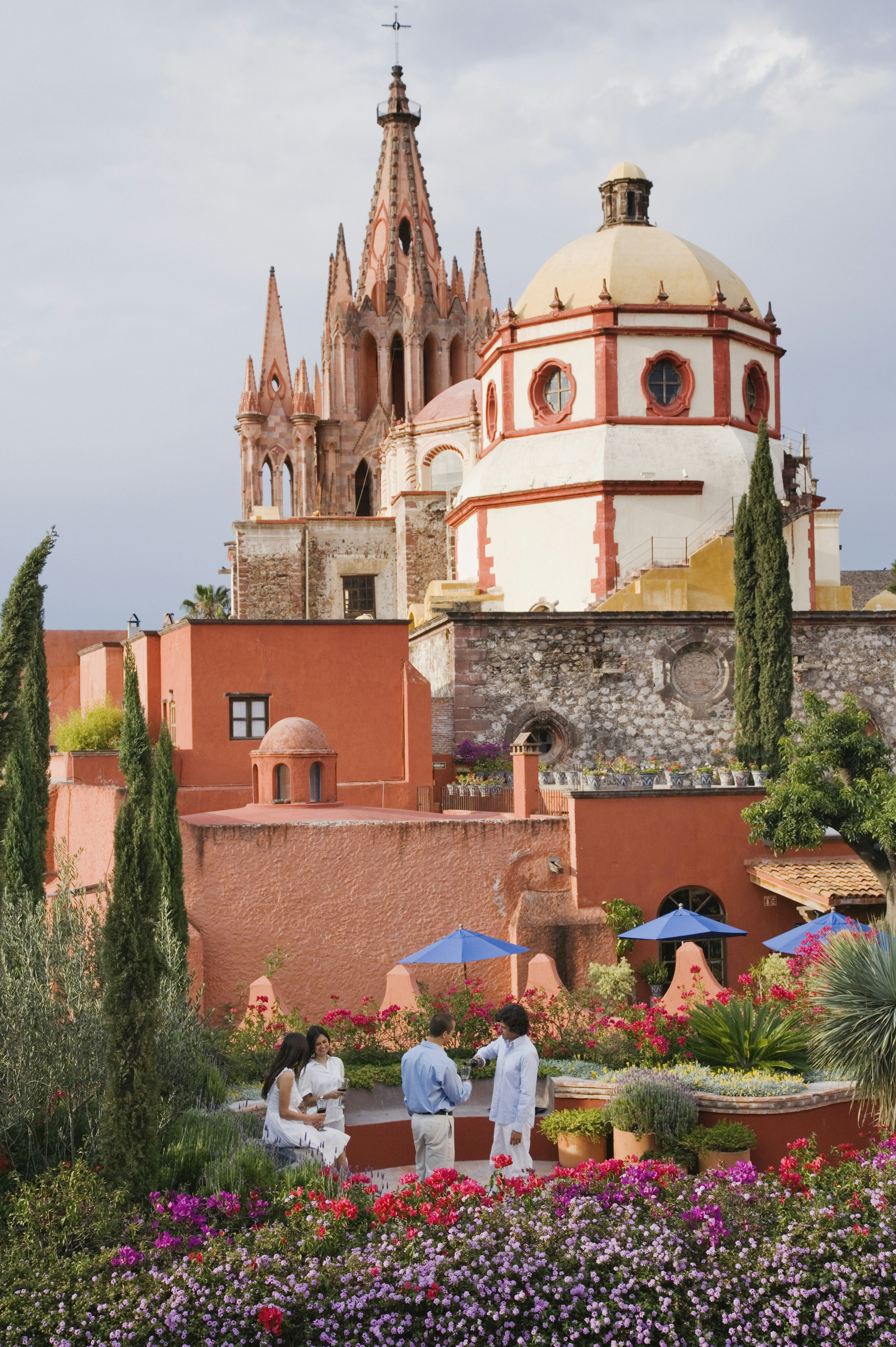 A white-dome in front of a spiky church spire, with a flower garden in front of it