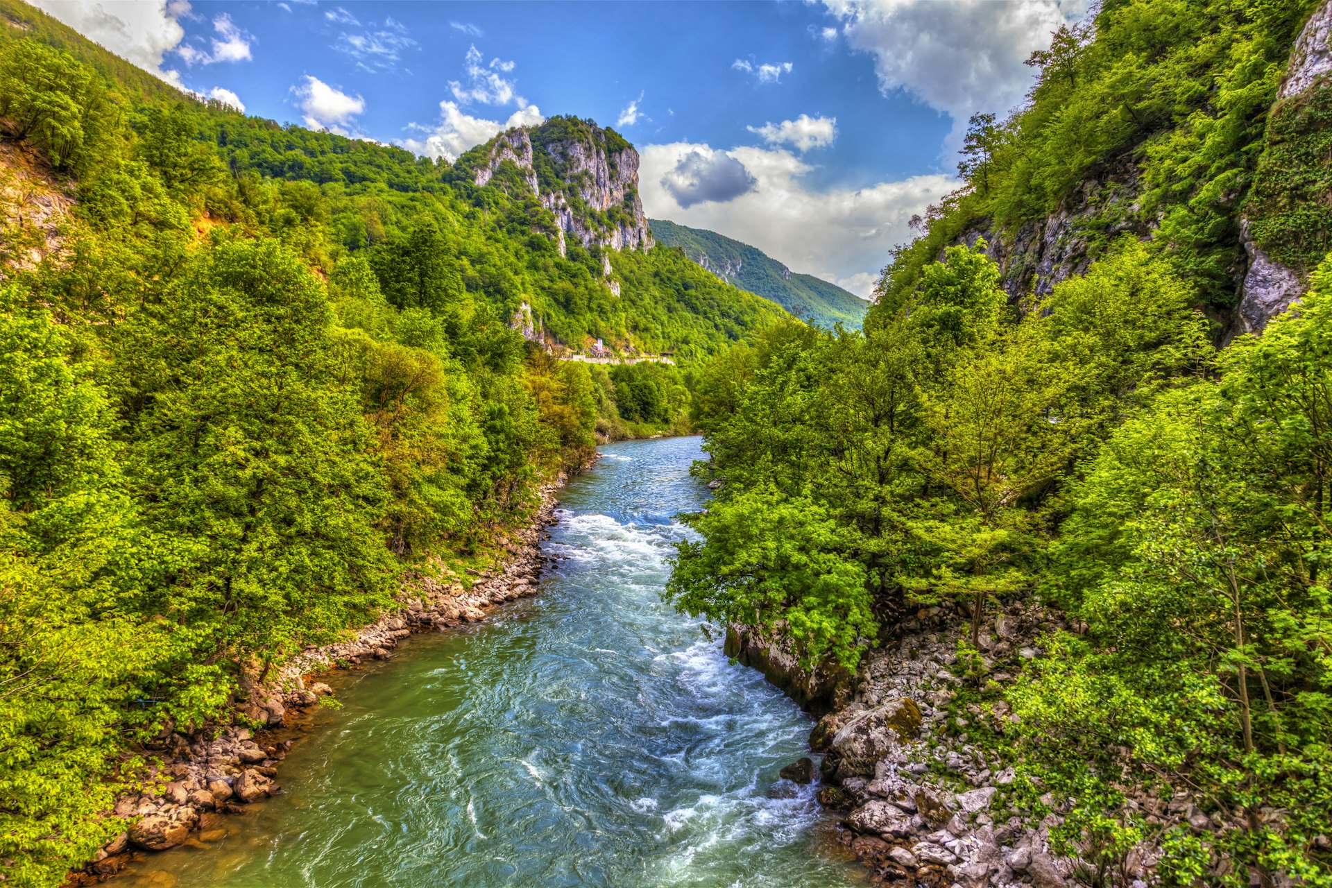 A fast-flowing turquoise river runs through a gorge on a sunny day