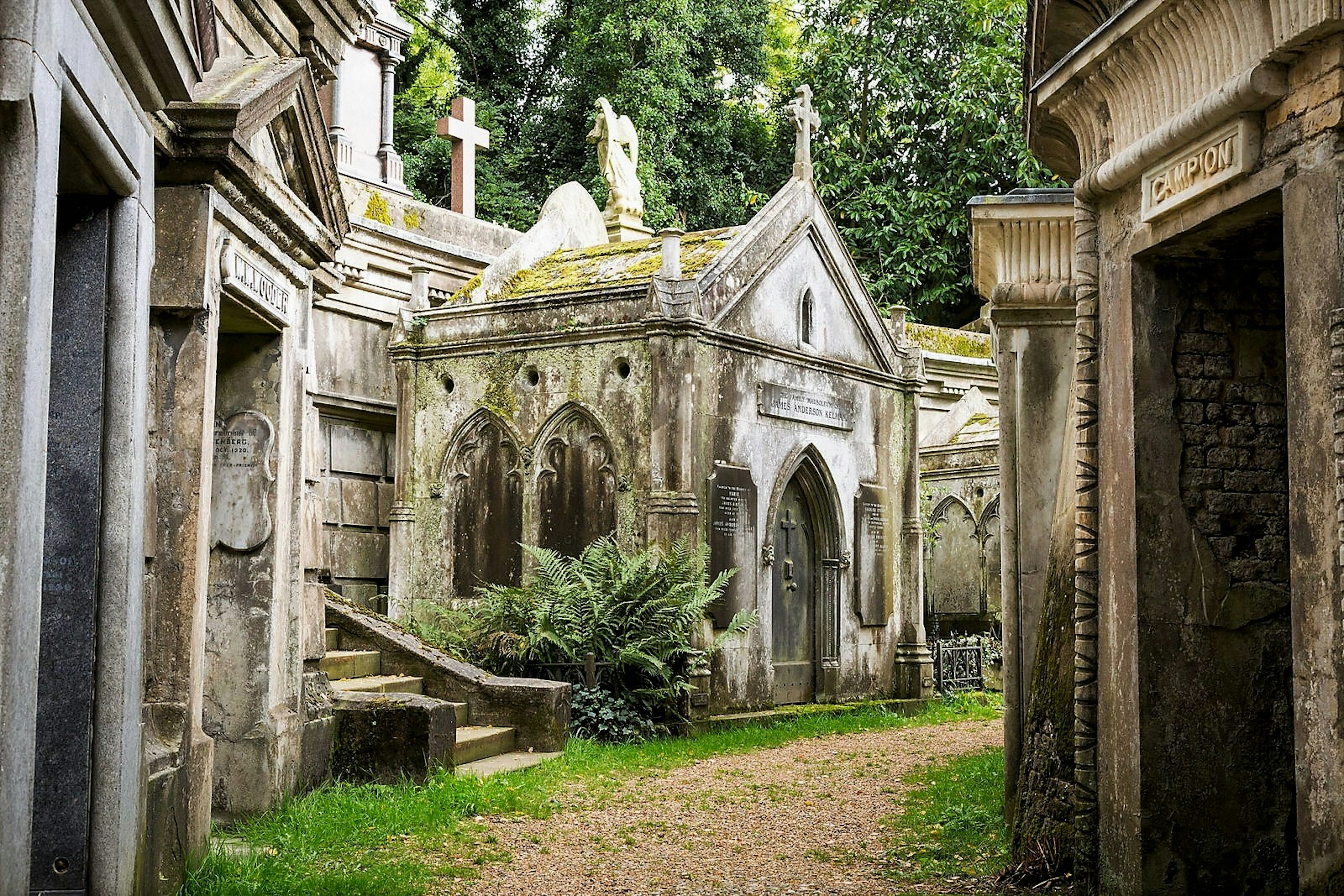 An old moss-covered stone mausoleum sits among a collection of other aging mausoleums in an old cemetery; London