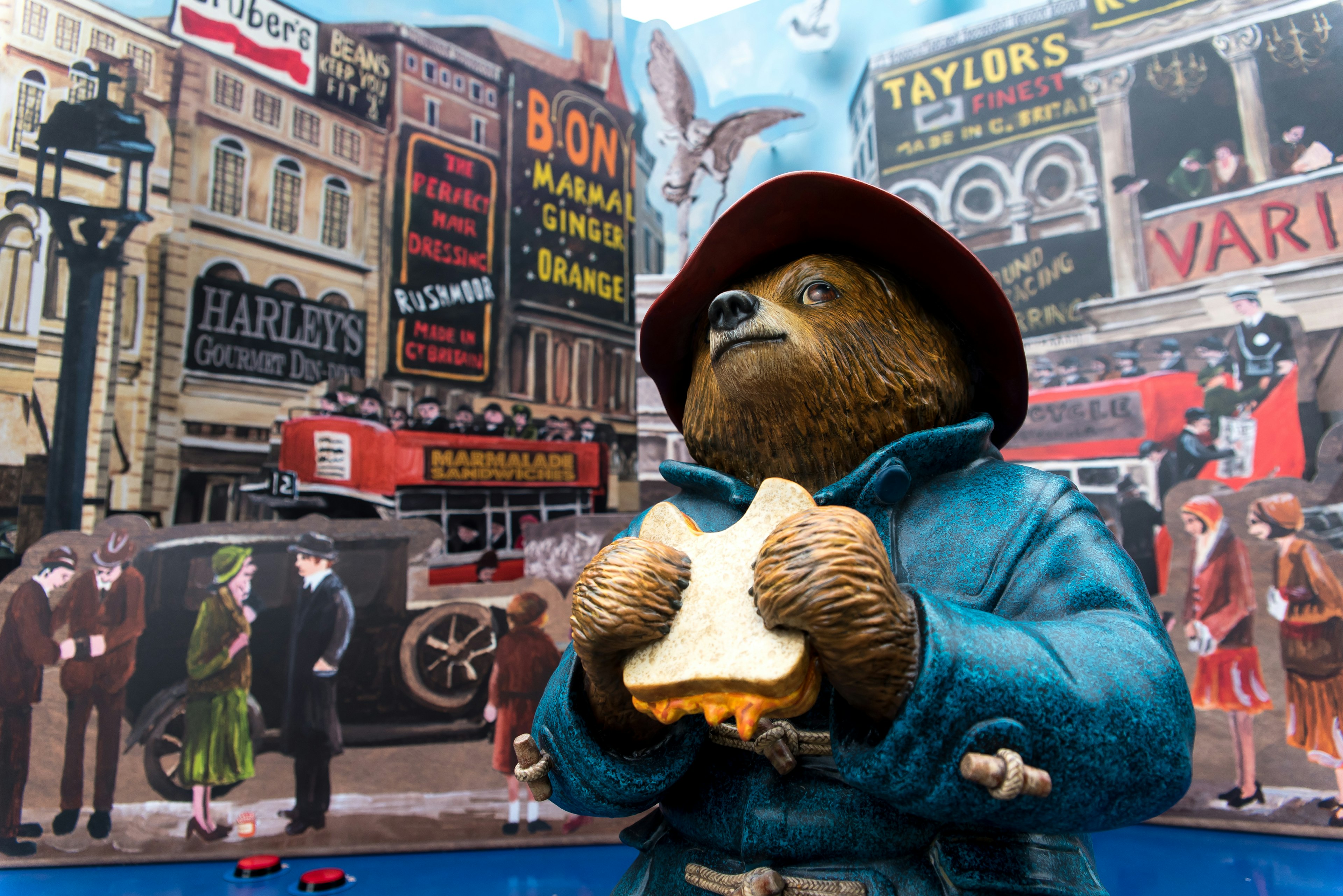 a bear in a red hat eats a sandwich while sitting on a bench