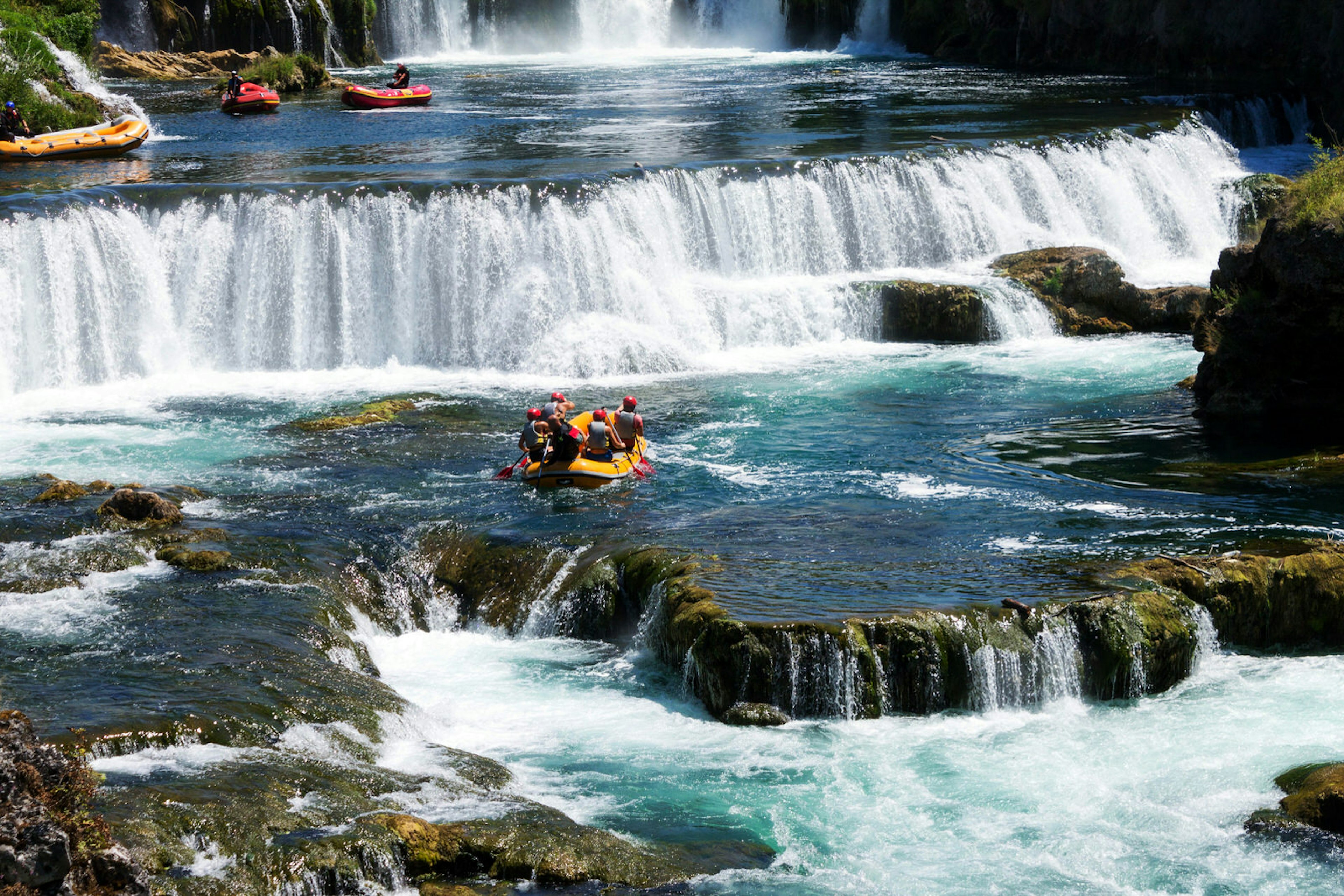 A small yellow raft is paddled towards a dramatic waterfall