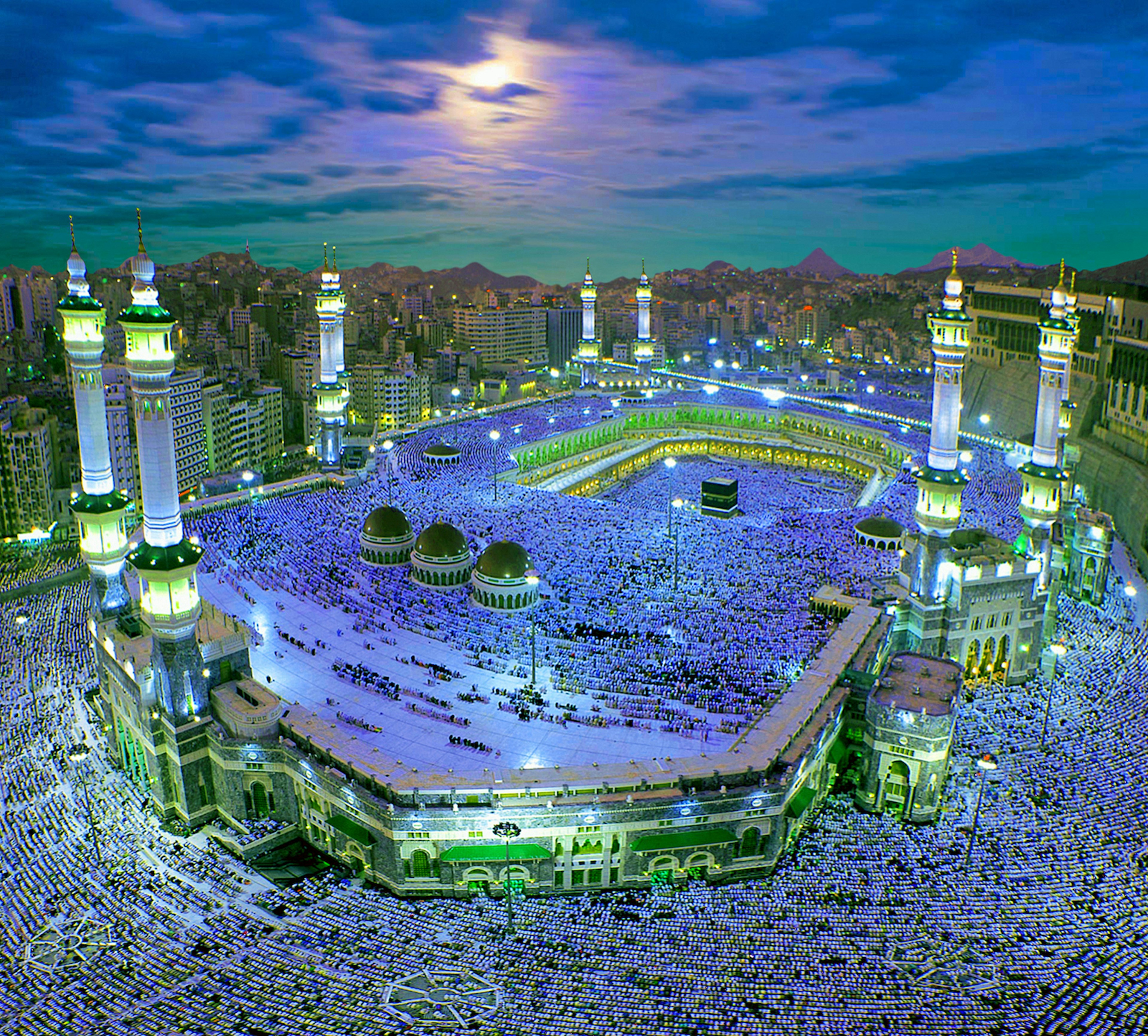 An overhead view of The Great Mosque of Mecca hosting millions of Muslim pilgrims. The majority of the attendees are wearing white robes and are on the ground in prayer, arranged in rows all pointing towards the Kaaba.