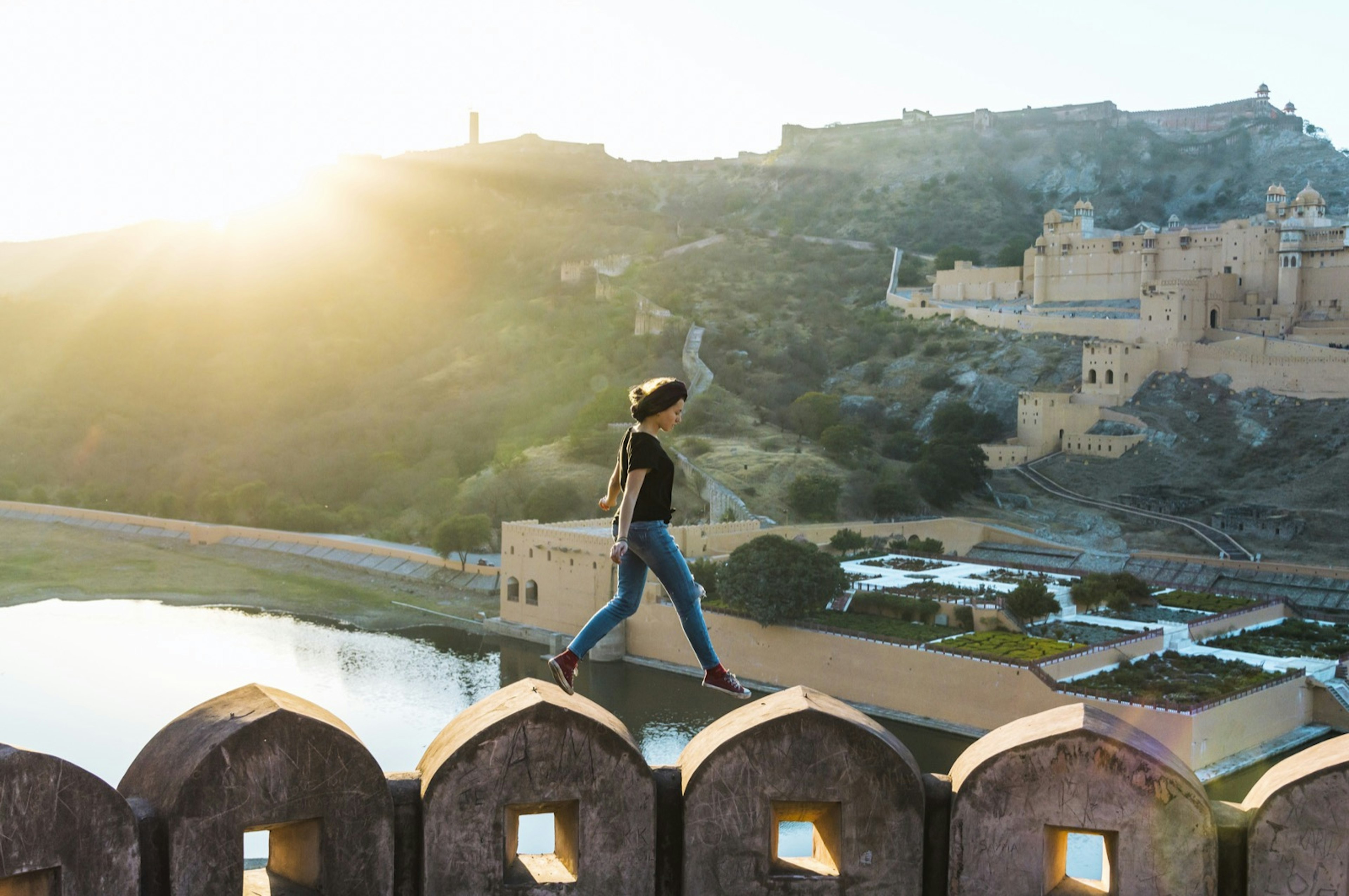 A woman walks over an arched wall with a walled city behind her; sacred spaces